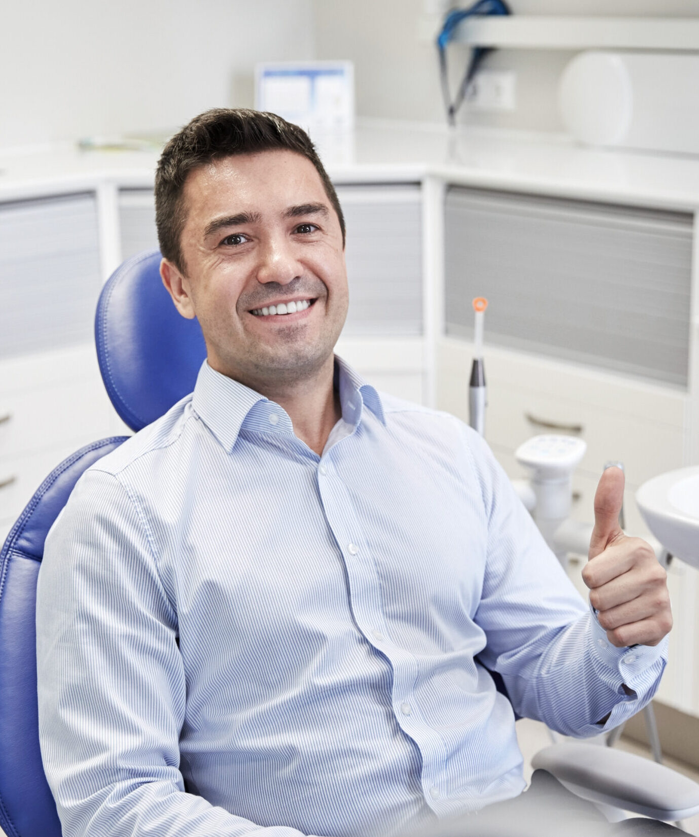 people, medicine, stomatology and health care concept - happy male patient sitting on dental chair and showing thumbs up at clinic office
