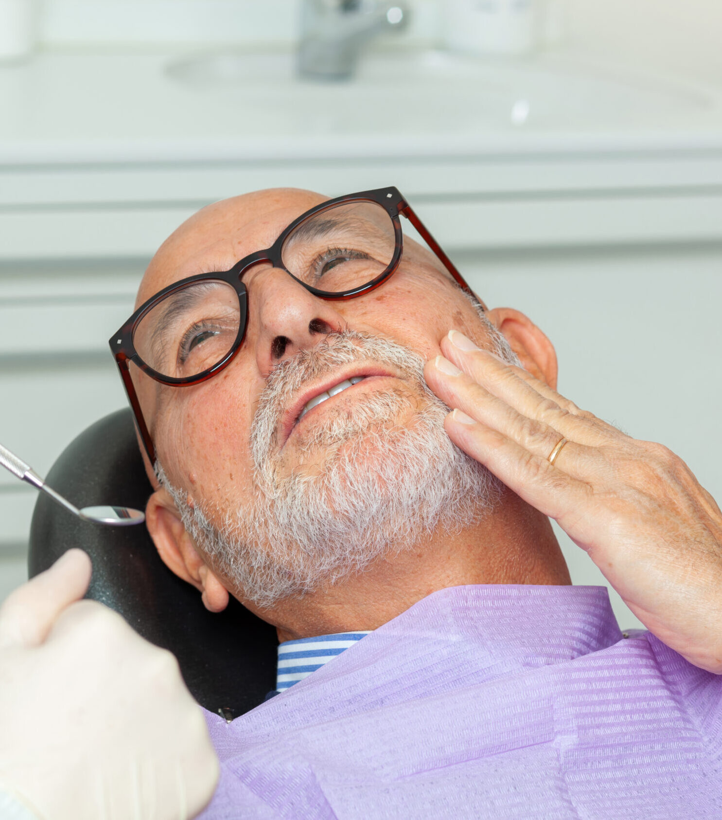 Senior man experiencing toothache during a dental checkup, showing signs of worry while undergoing examination in a clinic