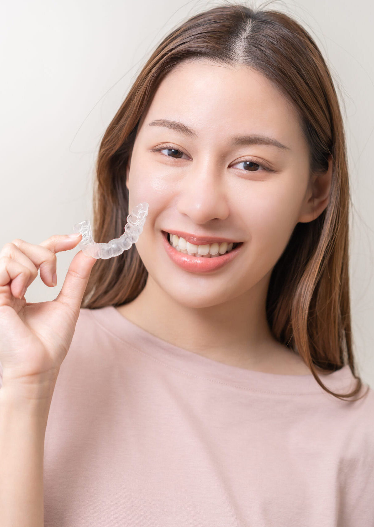 Dental invisible braces, beautiful smiling asian young woman holding invisalign braces, wearing orthodontic silicone trainer, white smile using invisible whitening tray. Stomatology, dental healthcare