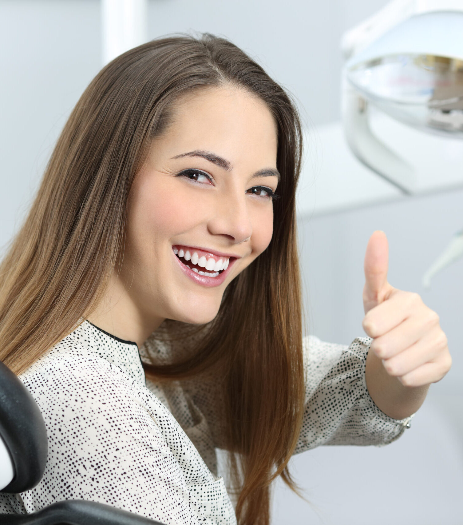 Patient with perfect white teeth and smile satisfied after dental treatment in a dentist office with medical equipment in the background