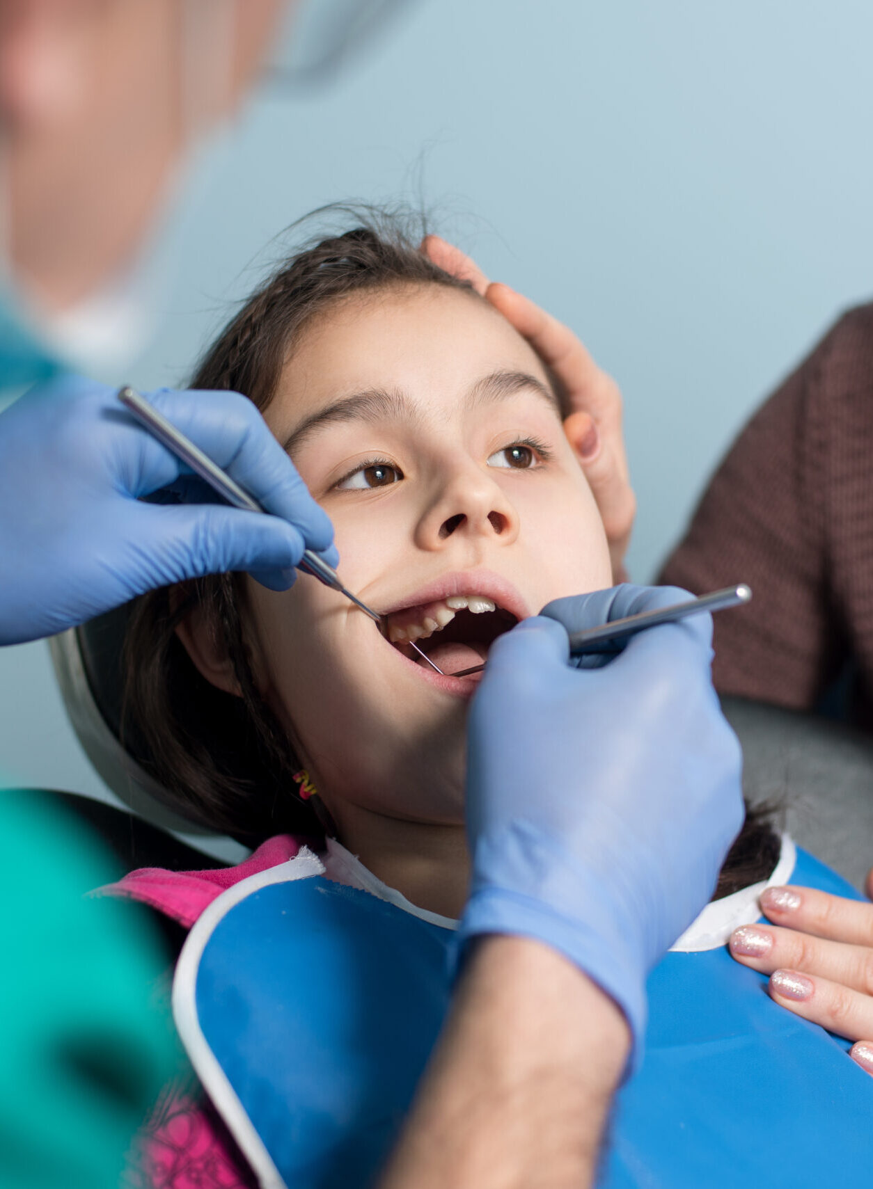 Young girl with mother on the first dental visit. Senior male dentist doing first check-up for patient at the dental office. Dentistry, medicine, stomatology and health care concept. Dental equipment