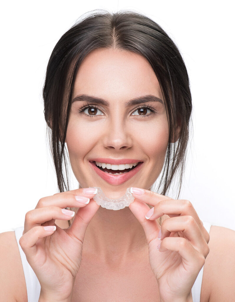 I want to adjust my teeth. Portrait of joyful girl wearing transparent orthodontic device for improving bite. She is standing and looking at camera with excitement. Isolated