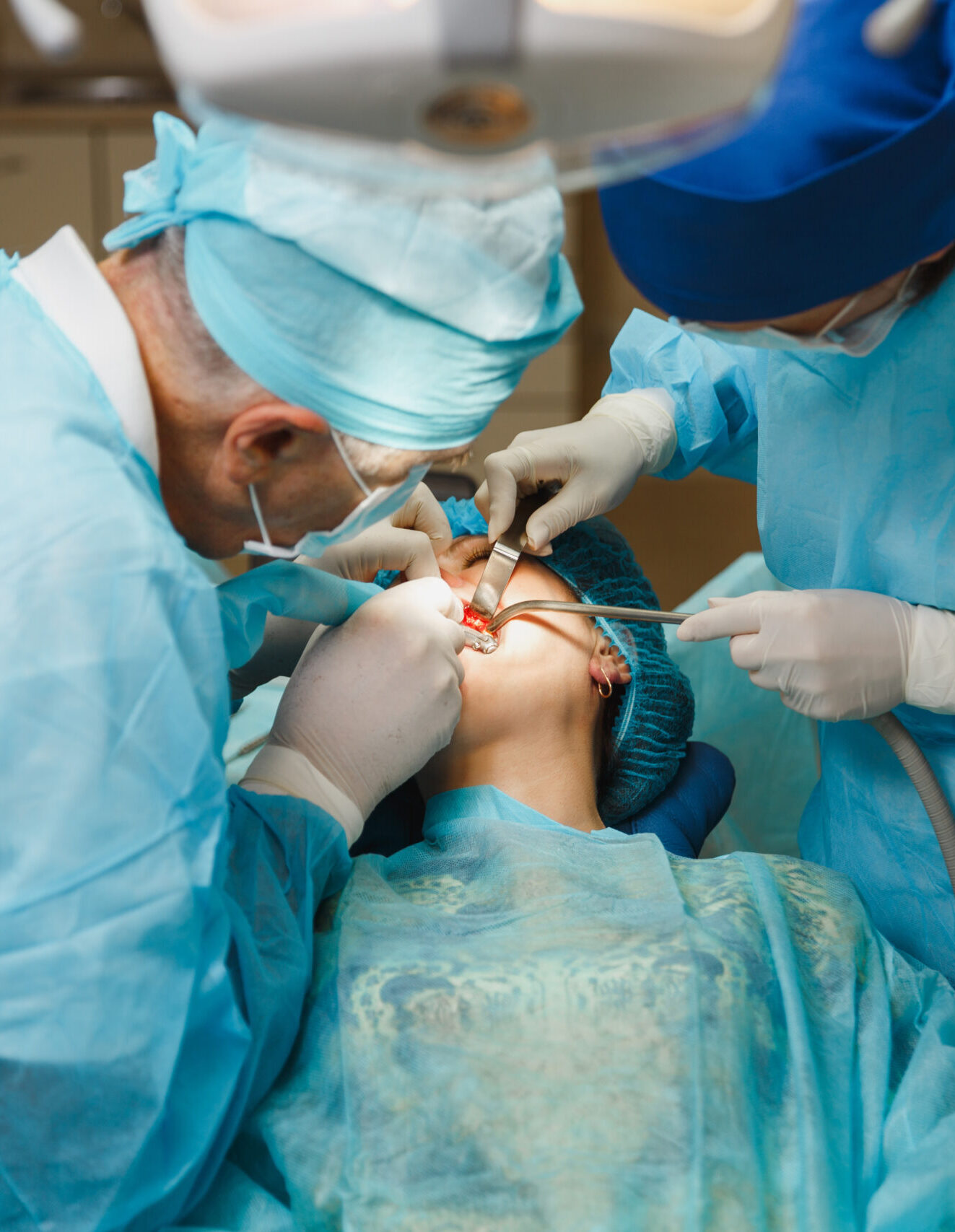 Male old professional dentist surgeon in uniform and female assistant helps to performing operation install dental implant teeth of woman patient in clinic light office with modern tools equipment