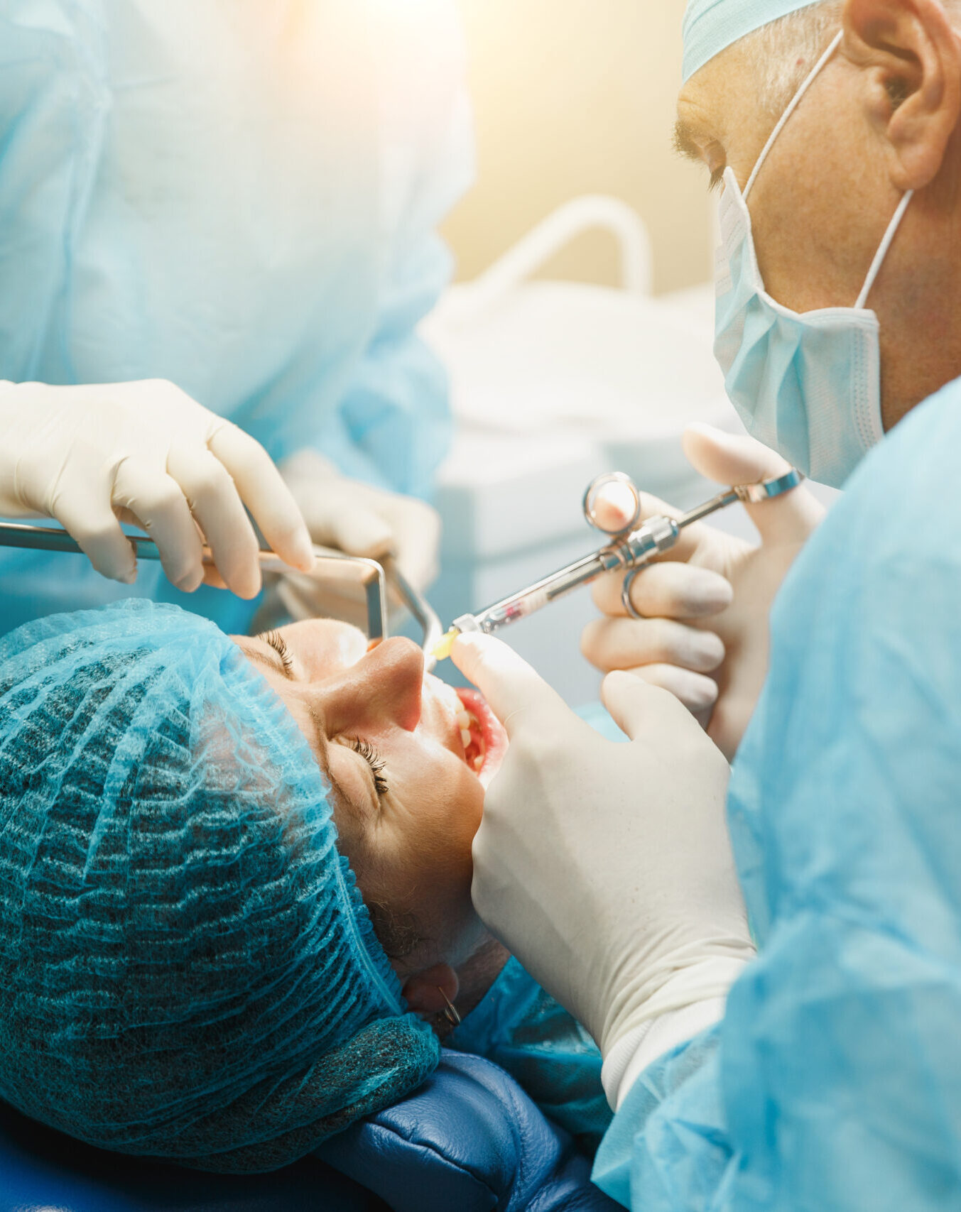 Male old professional dentist surgeon in uniform and female assistant helps to performing operation install dental implant teeth of woman patient in clinic light office with modern tools equipment