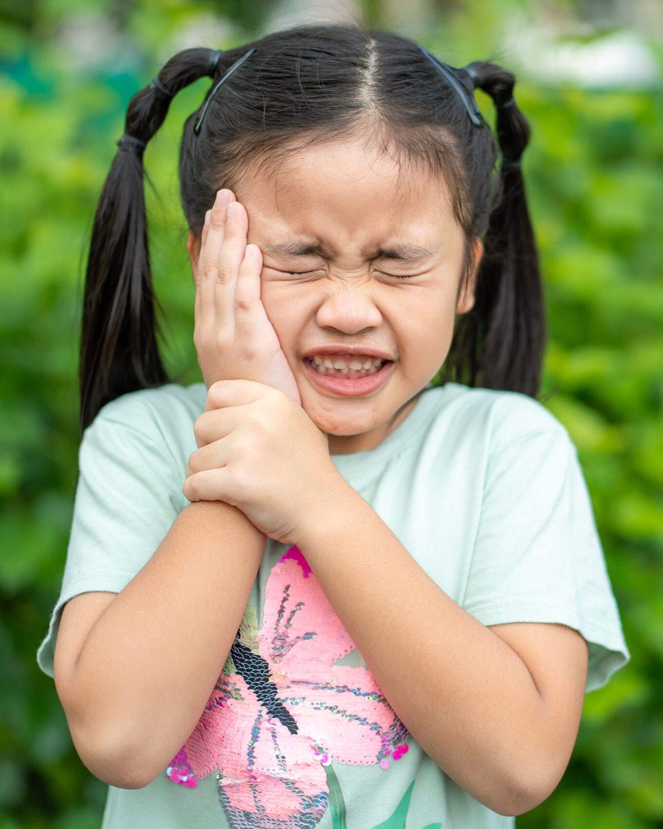 Tooth ache concept. Asian Little girl holding her cheek with hand, suffering from bad toothache. Kid with painful expression .Caries. a loose tooth, Severe tooth pain.