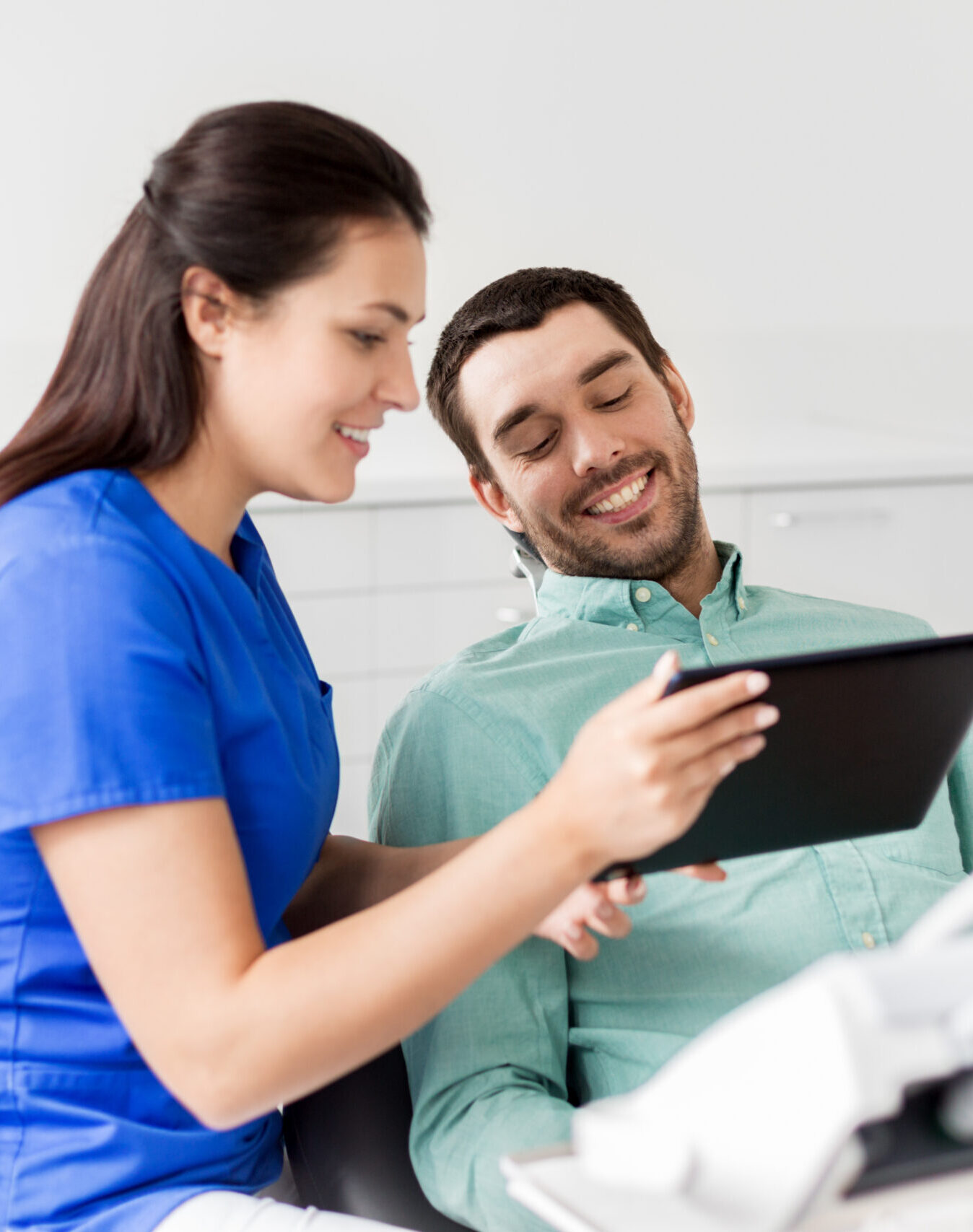 medicine, dentistry and healthcare concept - female dentist with tablet pc computer and male patient discussing teeth treatment at dental clinic office