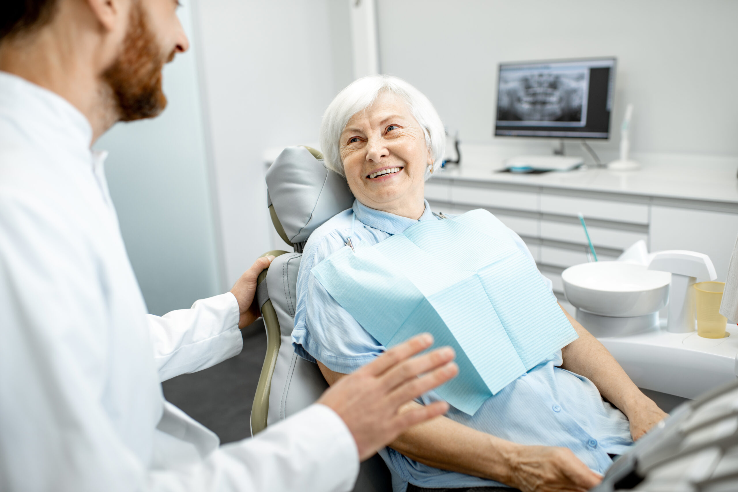 Beautiful elder woman with healthy smile sitting during the consultation with dentist at the dental office