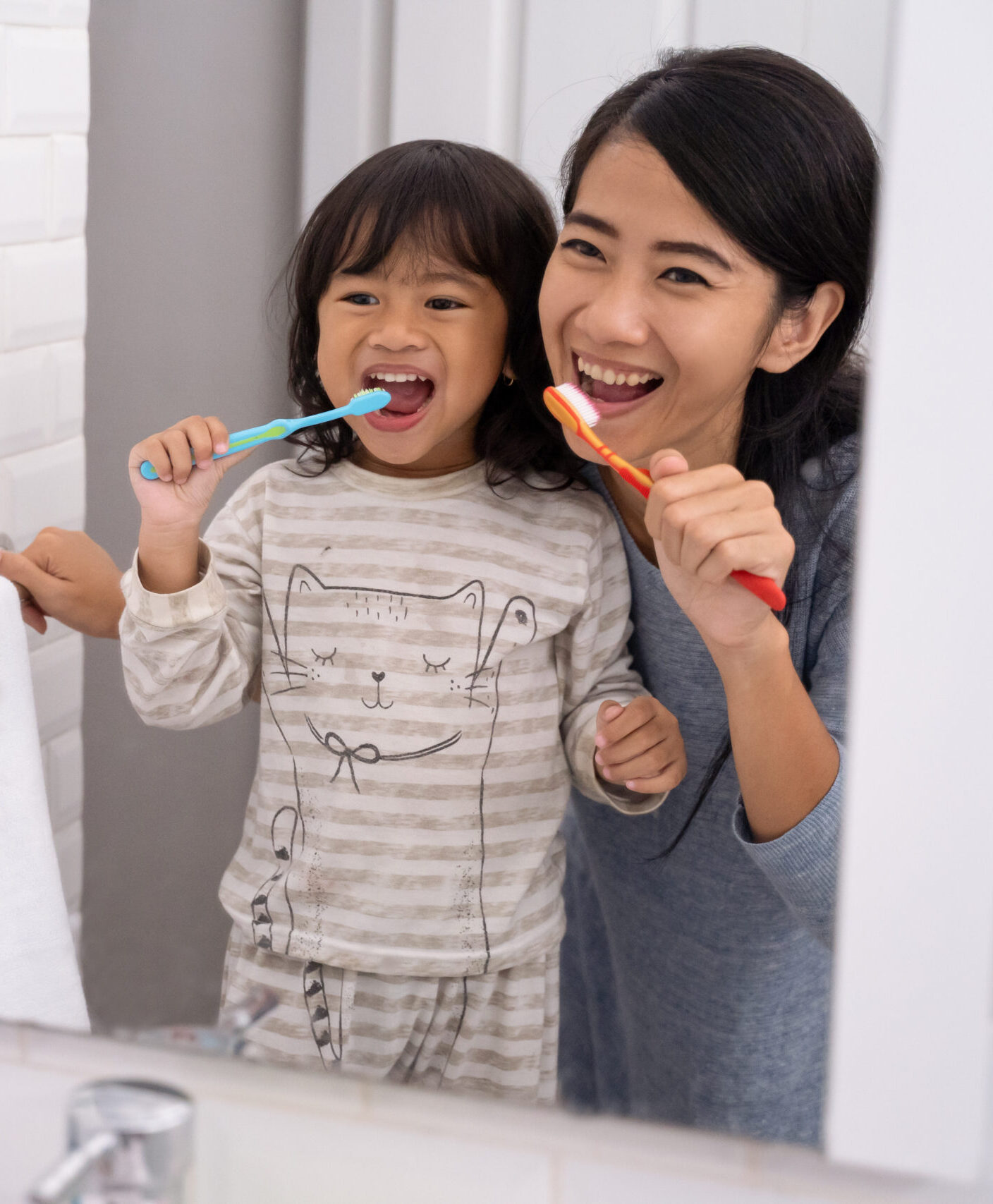 happy attractive mom and kid brushing their teeth together in bathroom sink in the morning
