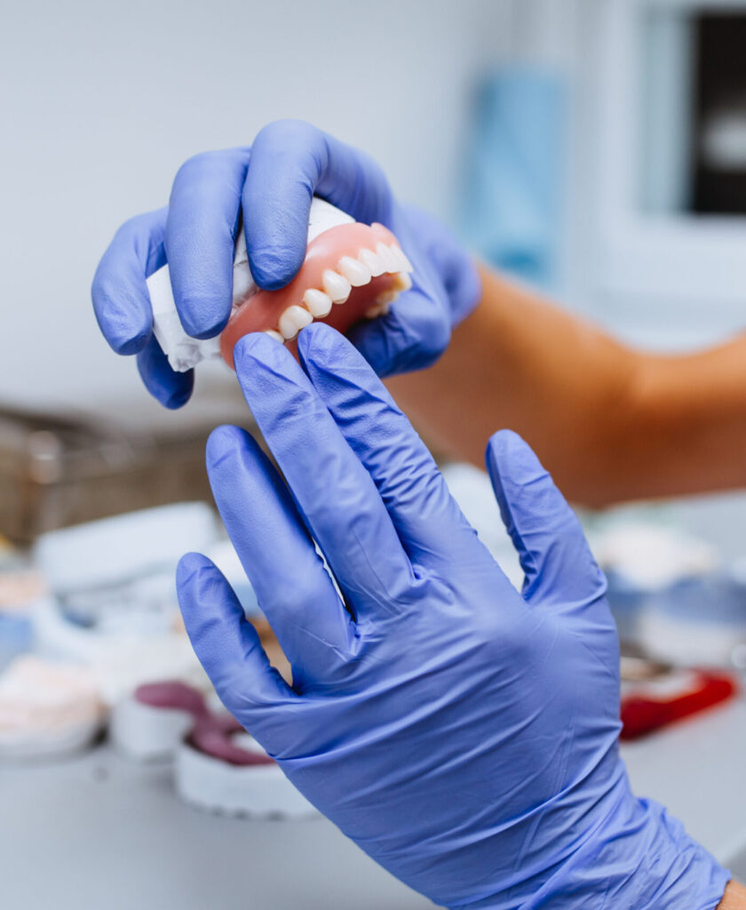 Dental prosthesis, prosthetics work. Close up of prosthetic's hands while working on the denture. Selective focus.