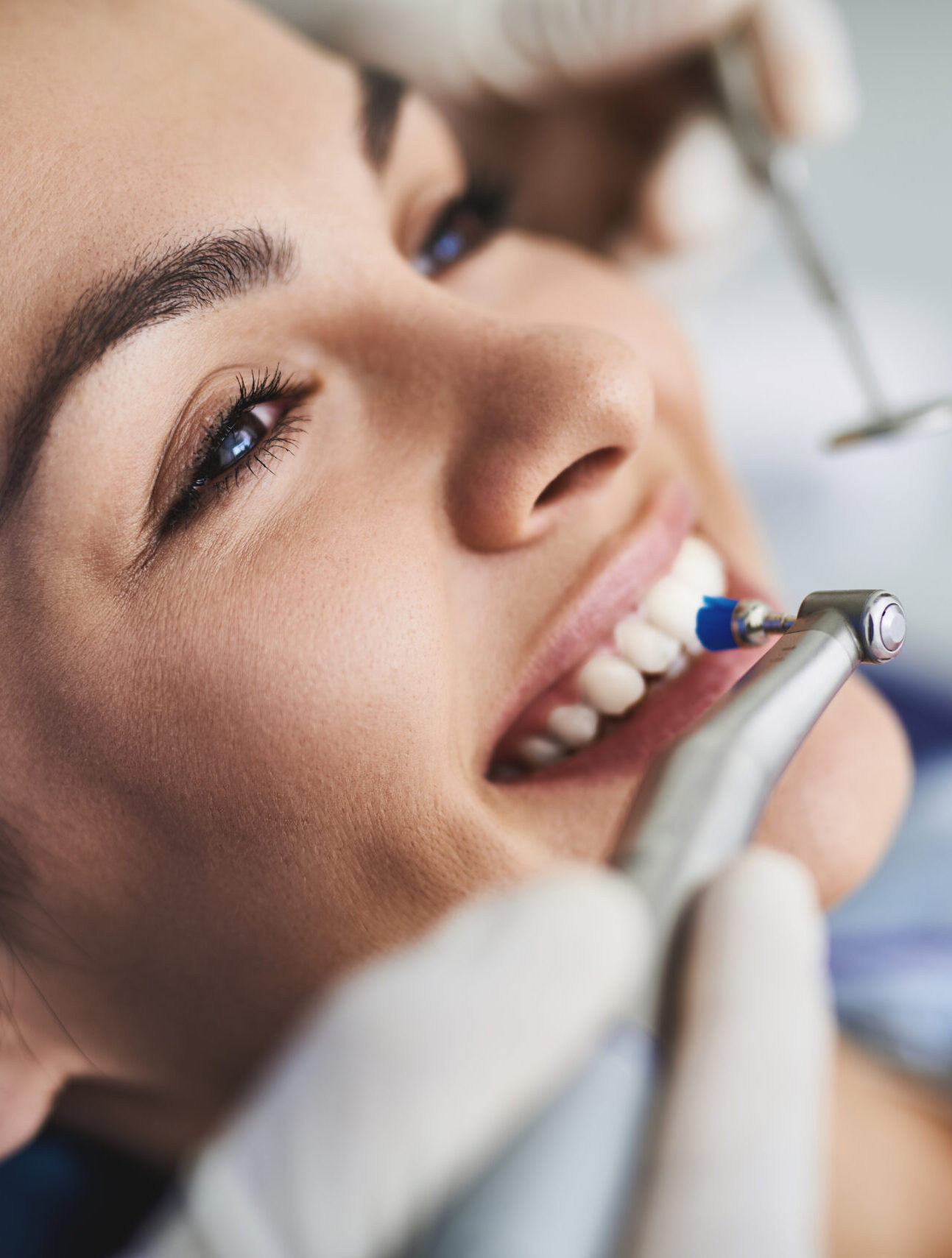 Close up portrait of pretty girl sitting in dental chair while stomatologist holding polisher and mirror. Girl is smiling