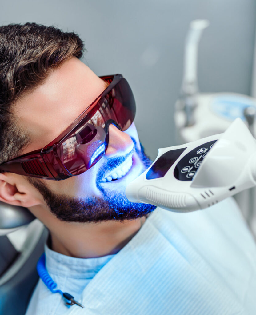 Dentist starting teeth whitening procedure with young man.