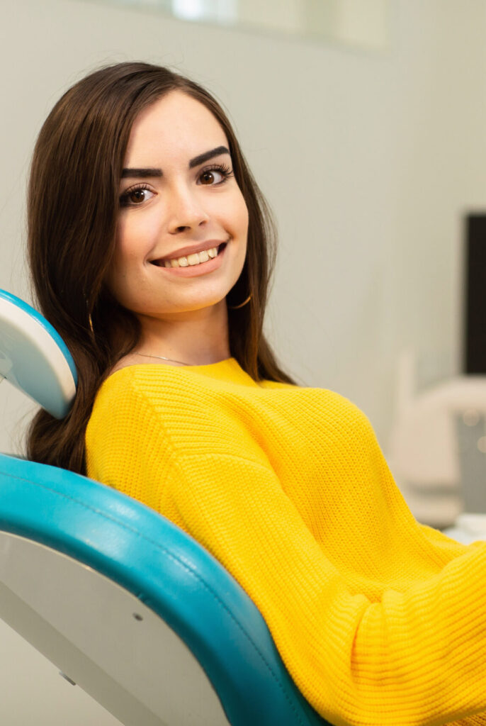 Young happy woman client looking at the mirror with toothy smile at the dental office.