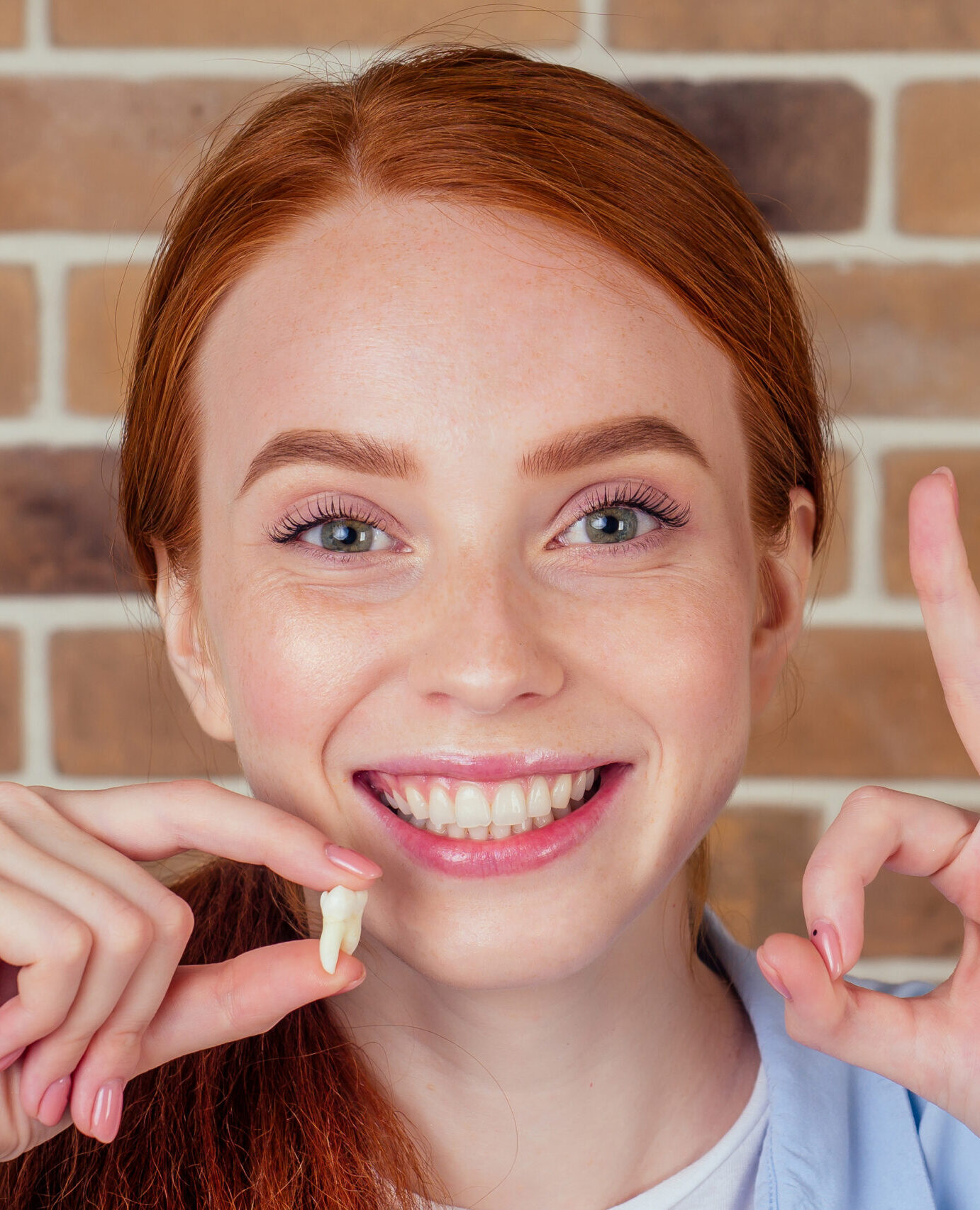 redhaired ginger female with snow-white smile holding white wisdom tooth after surgery removal of a tooth