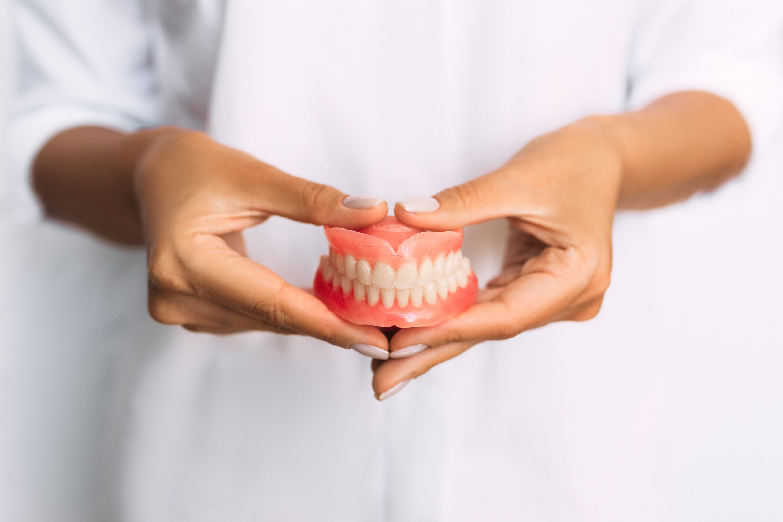 The dentist is holding dentures in his hands. Dental prosthesis in the hands of the doctor close-up. Front view of complete denture. Dentistry conceptual photo. Prosthetic dentistry. False teeth