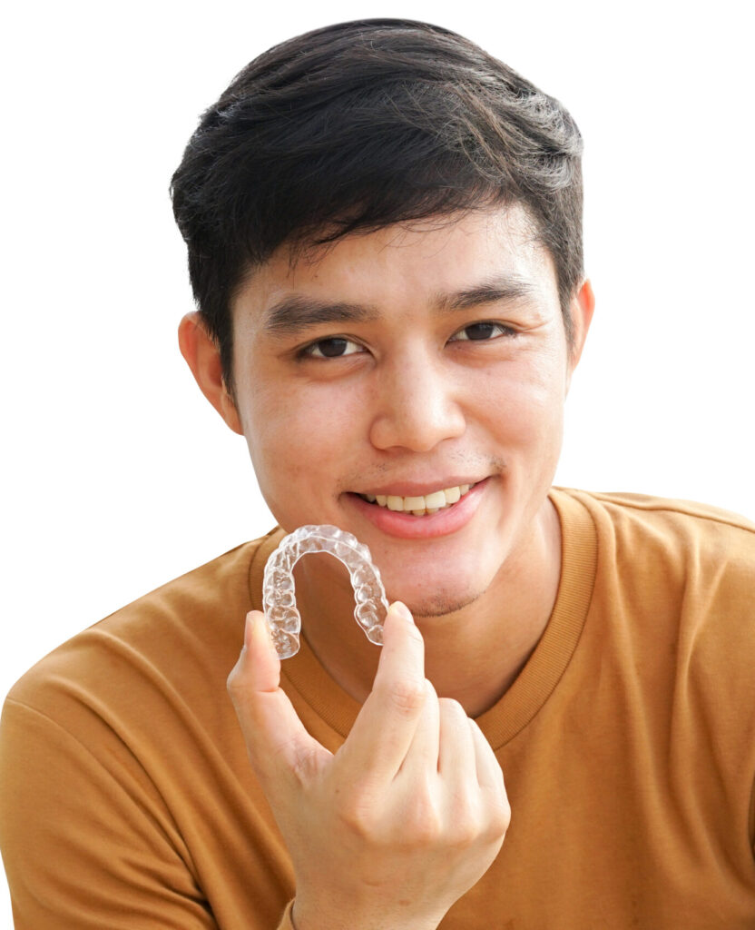 close up (isolated) young asian man smiling with hand holding dental aligner retainer (invisible) on white background of dental clinic for beautiful teeth treatment course concept