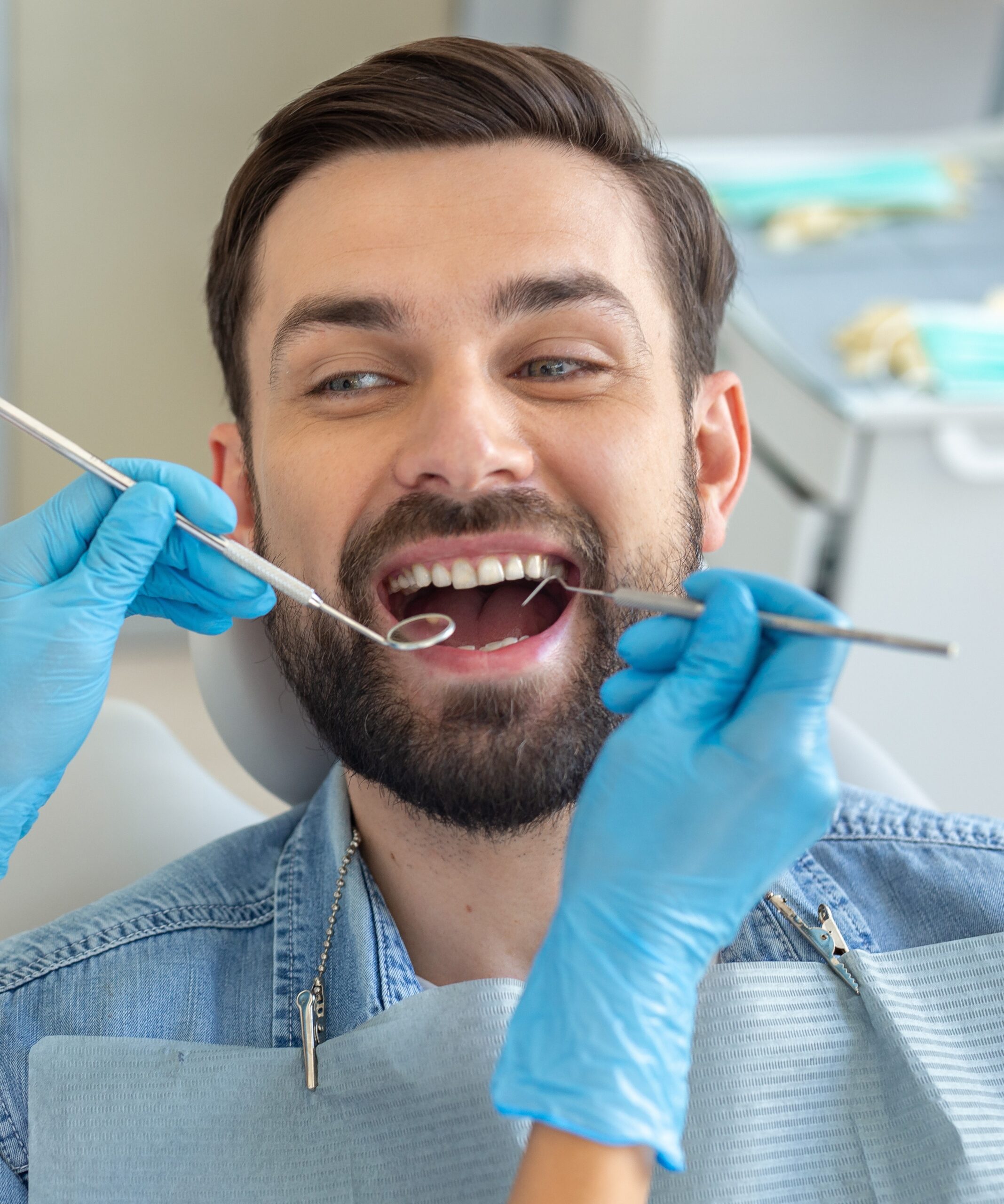 dentist examining teeth of handsome smiling client in dental chair