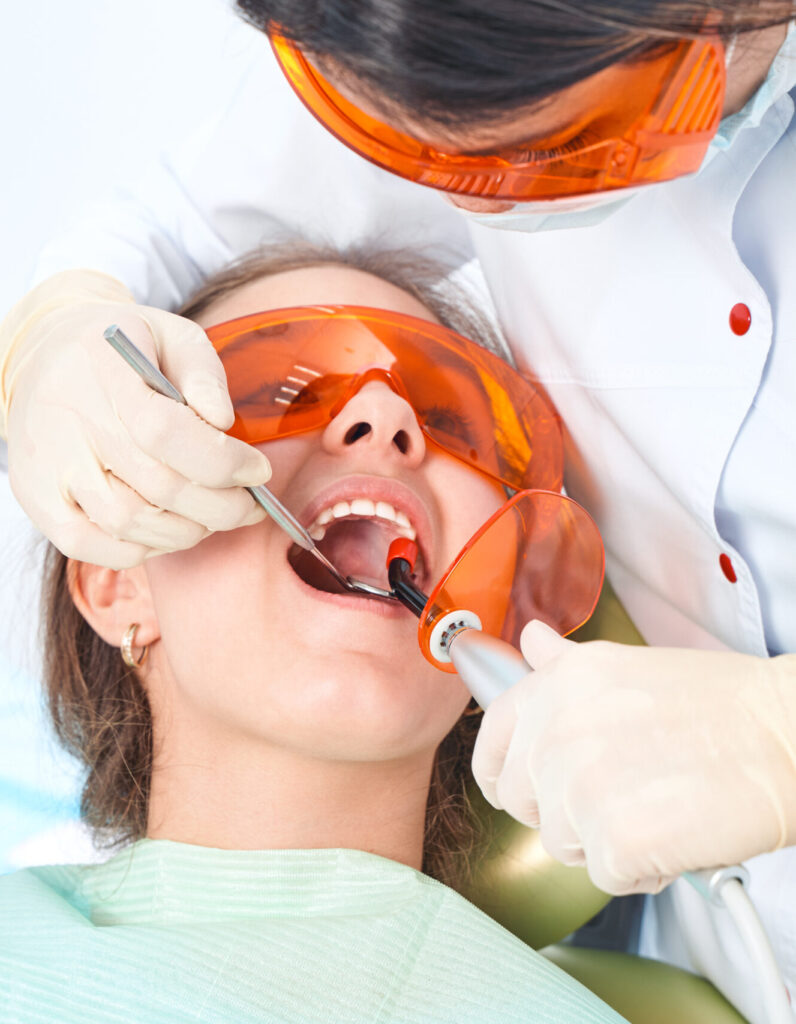 Girl child at the doctor. Dentist places a filling on a tooth with dental polymerization lamp in oral cavity. over clinic background.