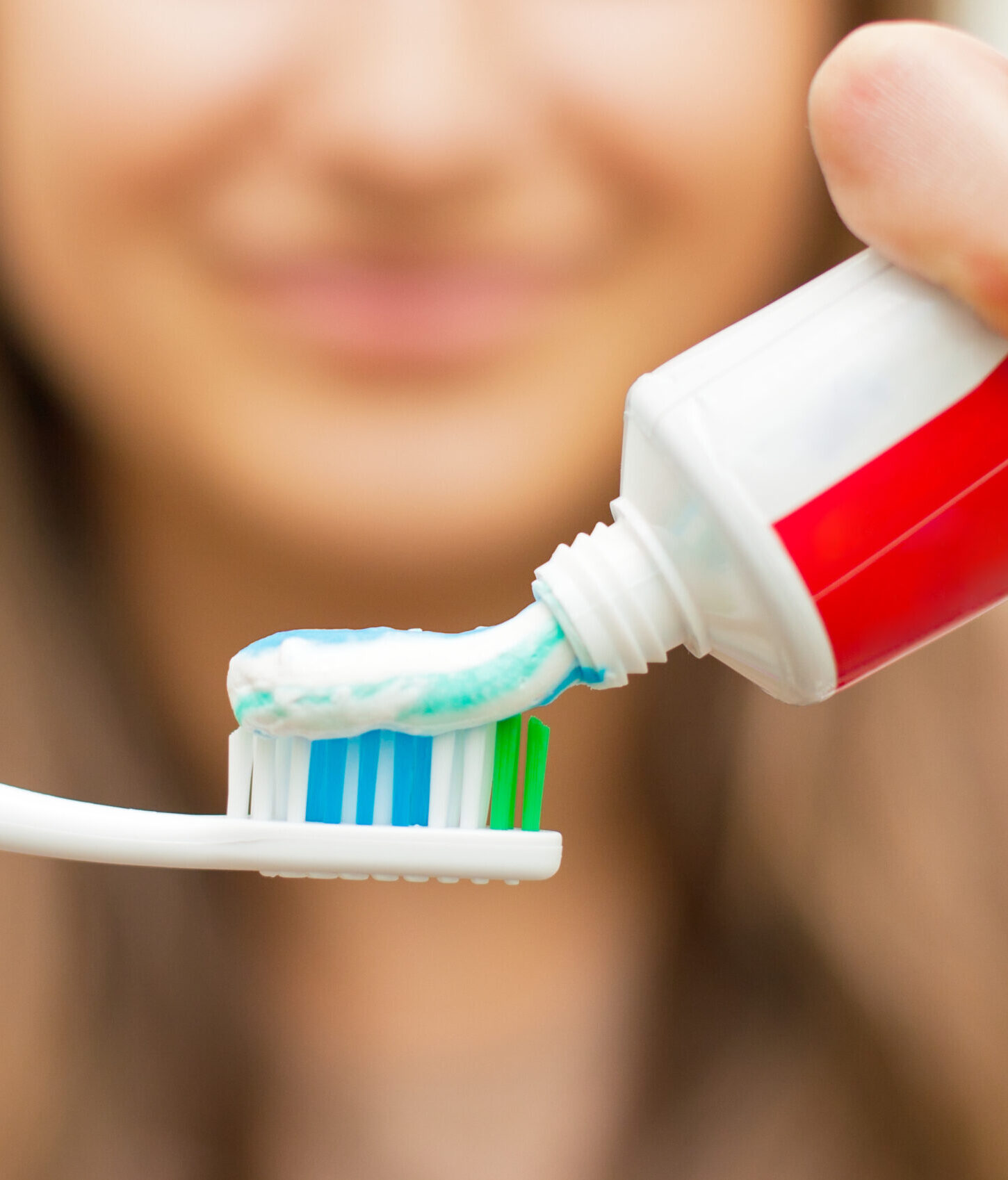 Young woman holding a toothbrush and placing toothpaste on it.