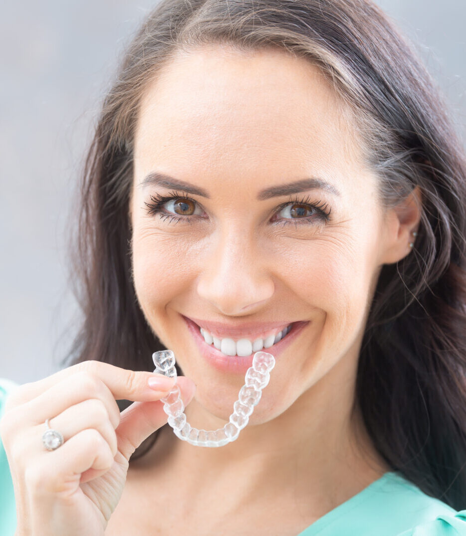 Invisalign orthodontics concept - Young attractive woman holding - using invisible braces or trainer.