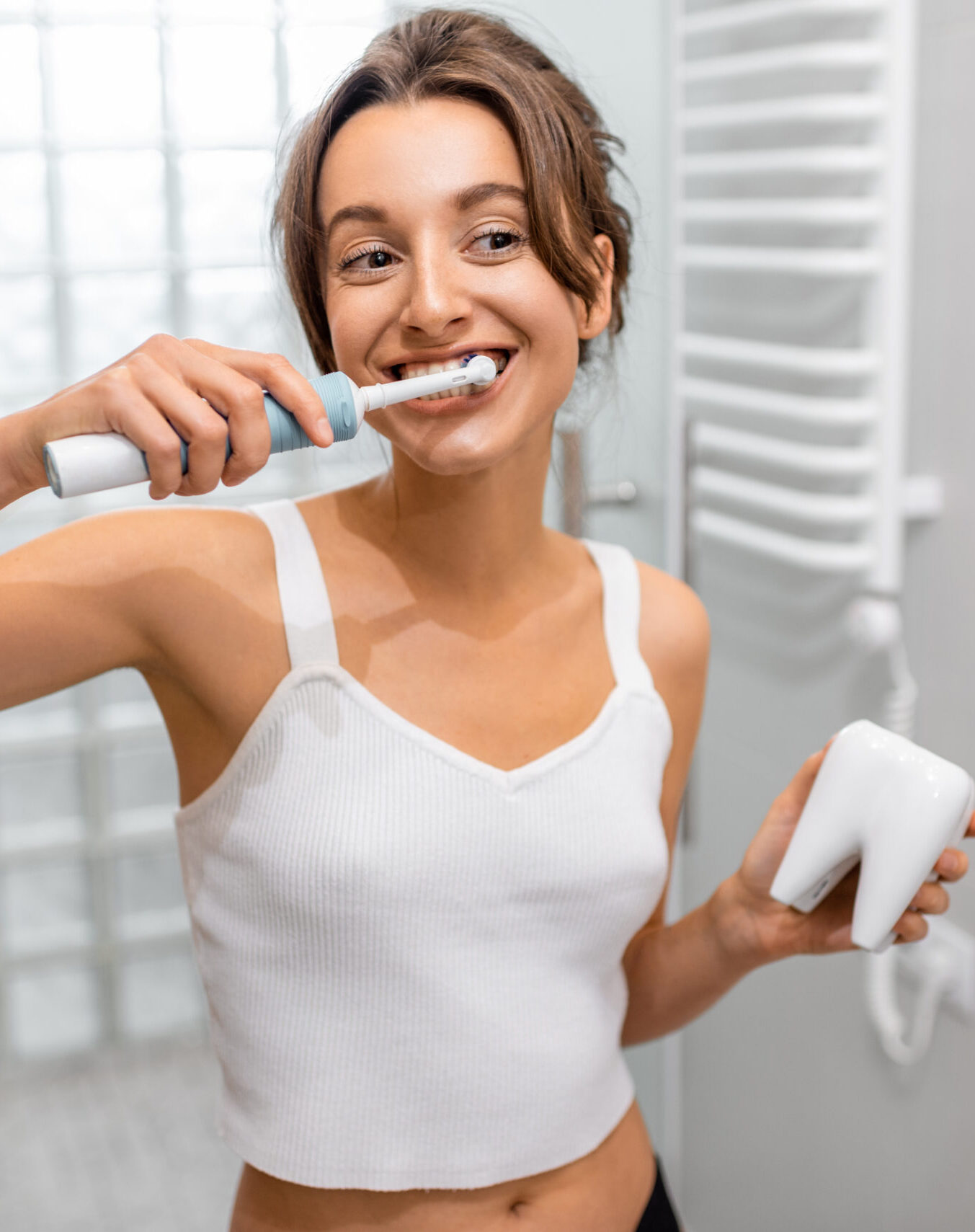 Young and cheerful woman brushing teeth with electric toothbrush during morning hygiene procedures in the bathroom