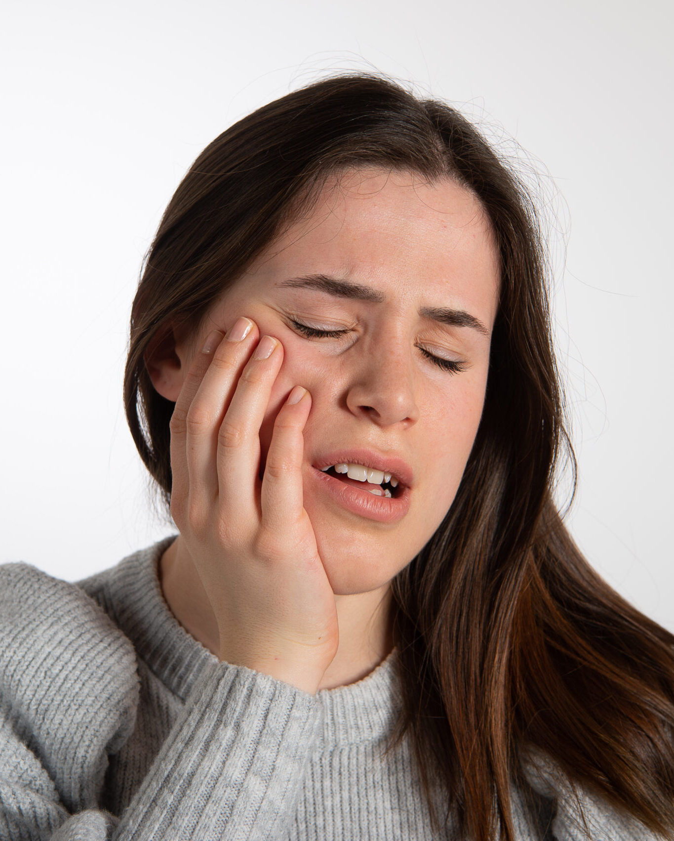 Painful facial expression of a young woman with tooth ache holding her check in agony. Dental health prevention concept