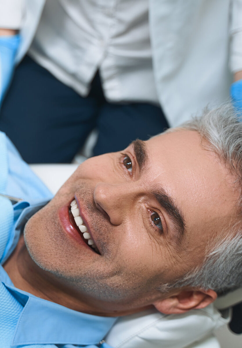 Joyful male is lying in chair and looking into mirror while being delighted with dentist work