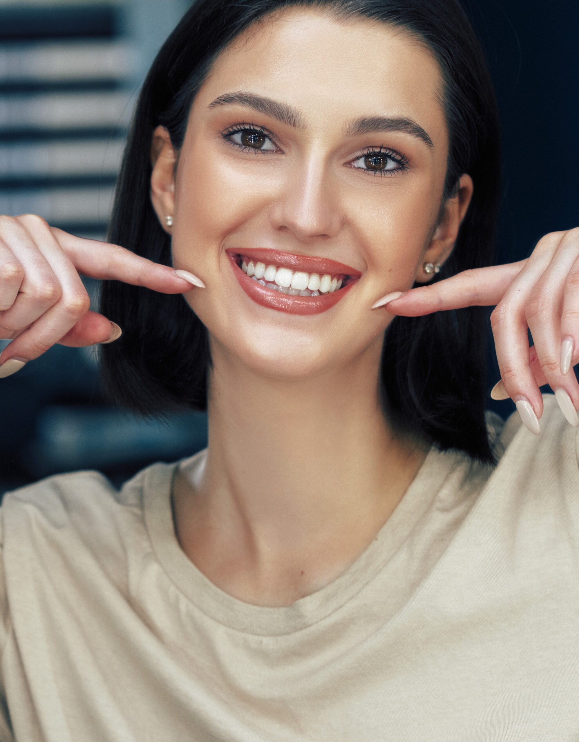 Portrait of a positive attractive girl with natural makeup smiling and showing with index fingers her healthy white teeth. Pretty young woman has joyful expression after makeup.
