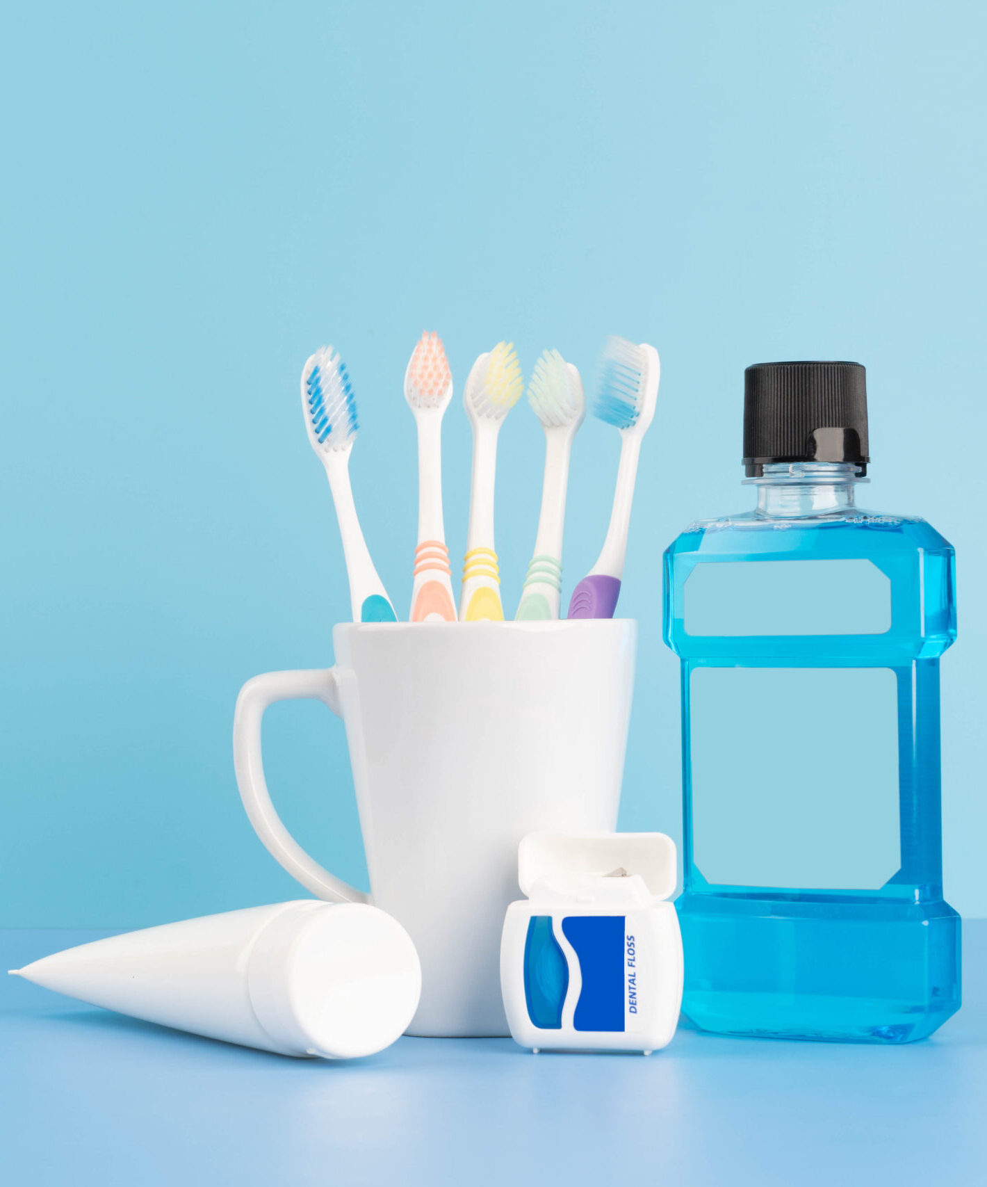 Oral care products set for healthy teeth and gums. Toothbrushes in glass with toothpaste, mouthwash and dental floss on blue background. Copy space.
