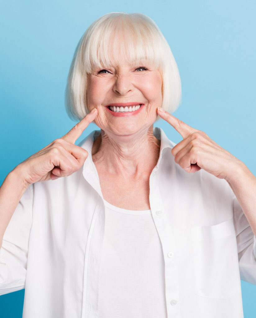 Photo portrait of granny blonde hair pointing at white teeth healthy smile dental whitening veneers isolated on bright blue color background.