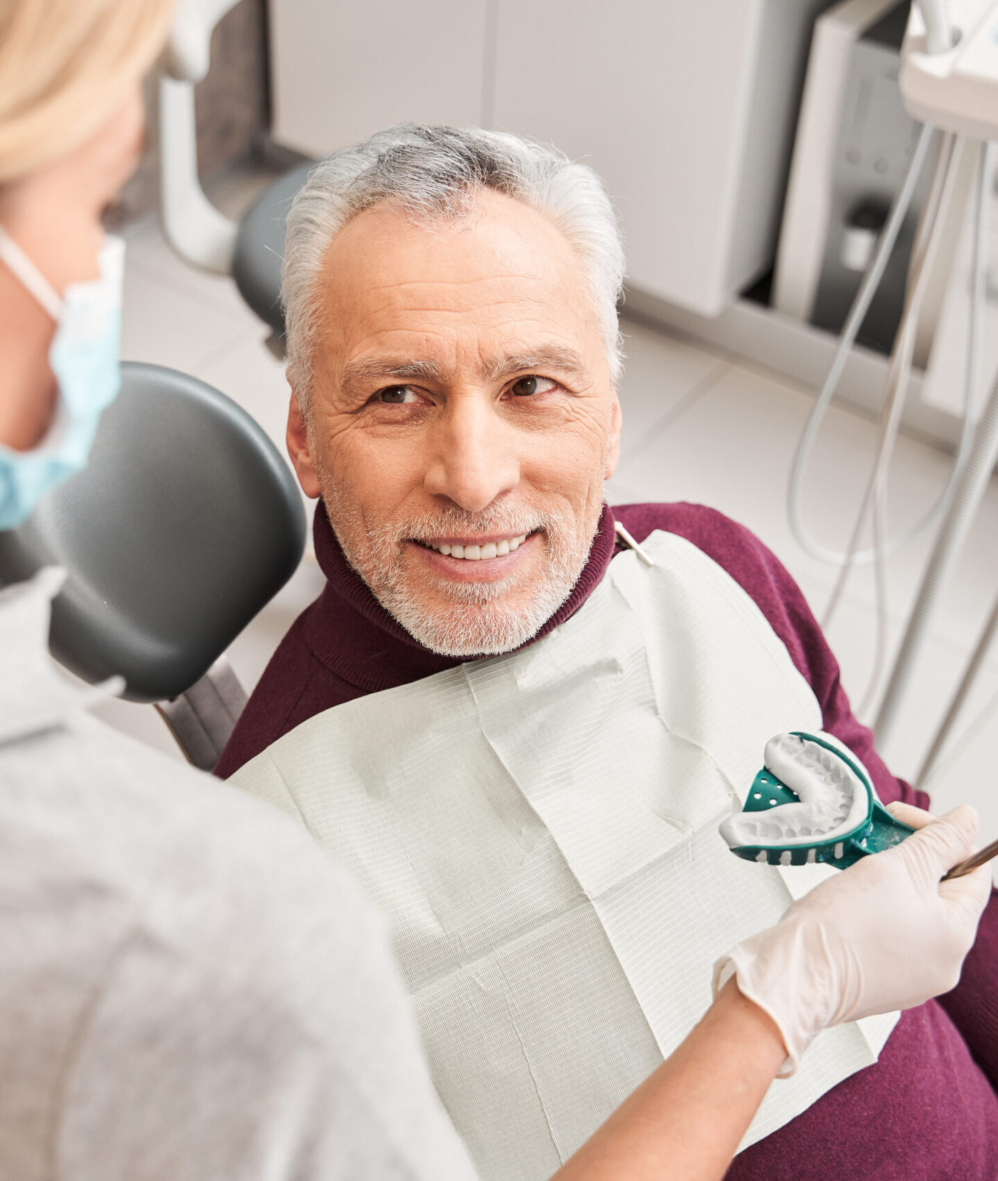 New smile. Back view of the female blonde caucasian doctor presenting dental impression for dentures to the senior smiling man. Stock photo