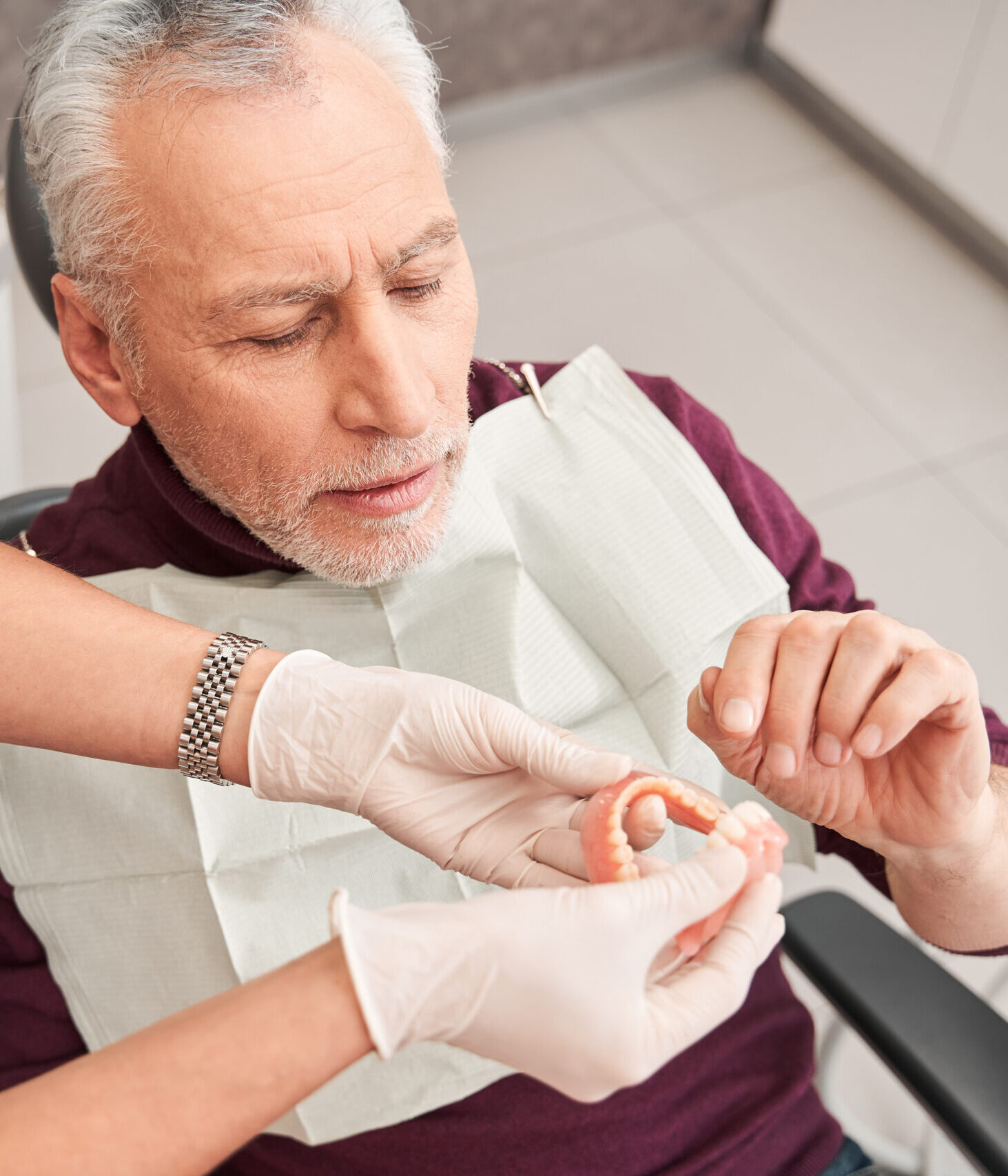 Cropped view of the young attractive woman doctor holding dentures or artificial teeth for man while talking about it to her client. Stock photo
