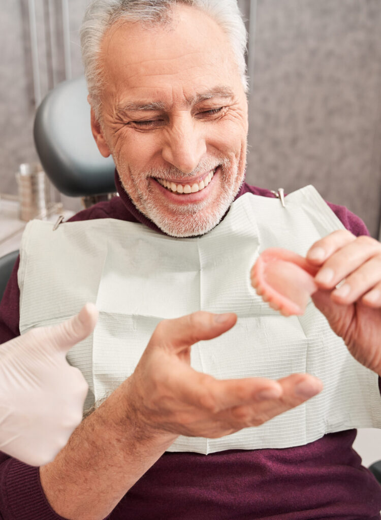 My new teeth. Cropped view of the dentist showing to senior grey haired patient teeth dentures while working at the dental clinic. Man sharing satisfaction smile