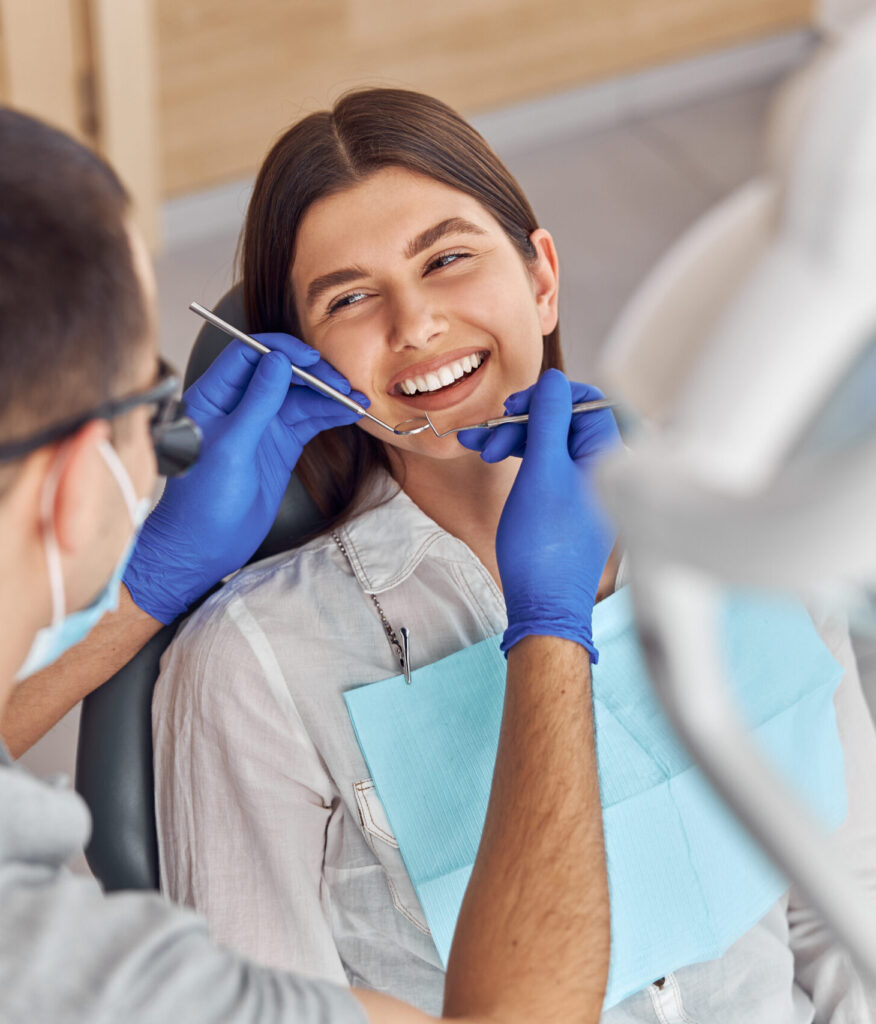 Cheerful positive dentist and client in dentistry. They look at each other and smile. Female client sit in chair.