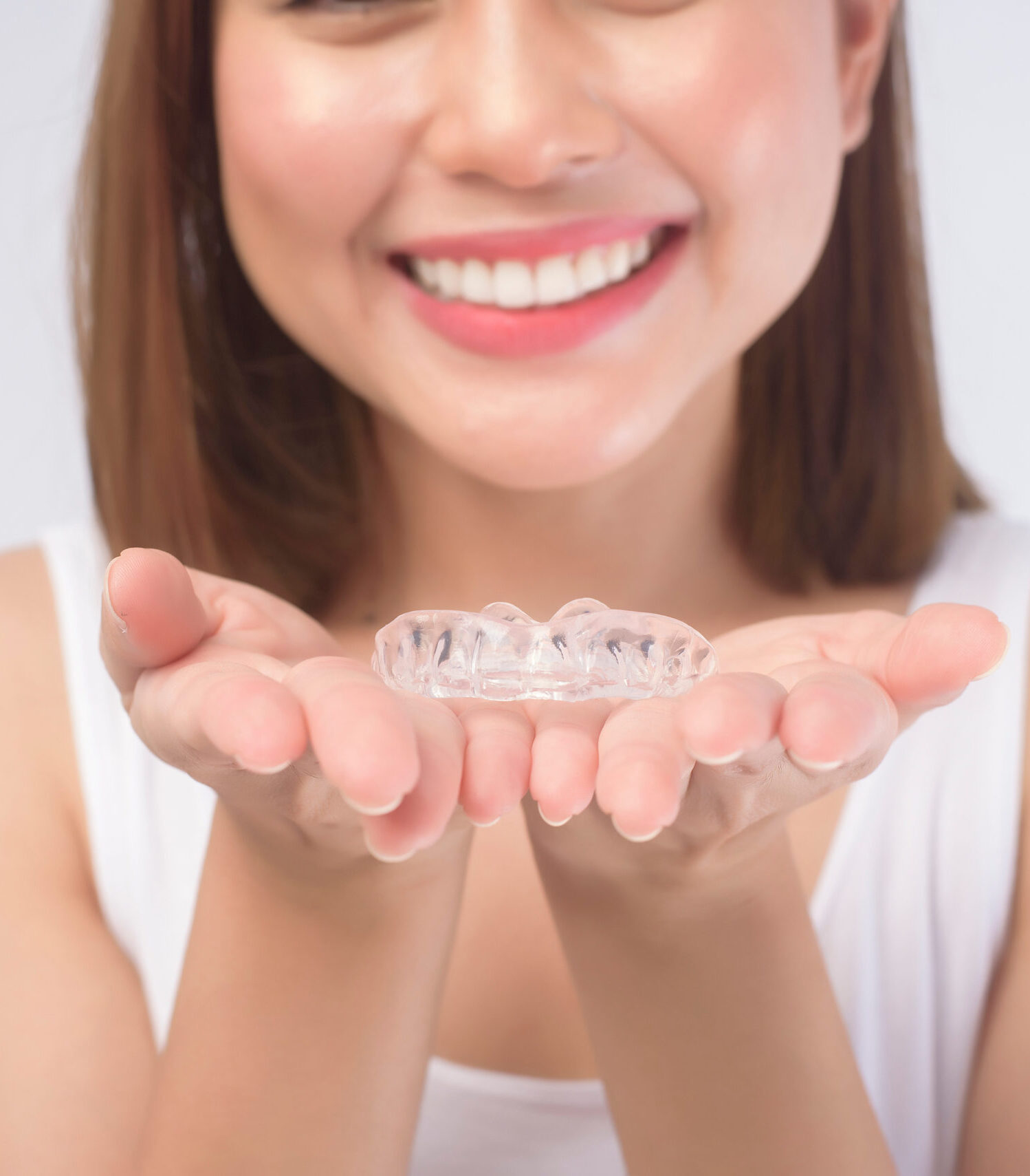 A young smiling woman holding invisalign braces over white background studio, dental healthcare and Orthodontic concept.