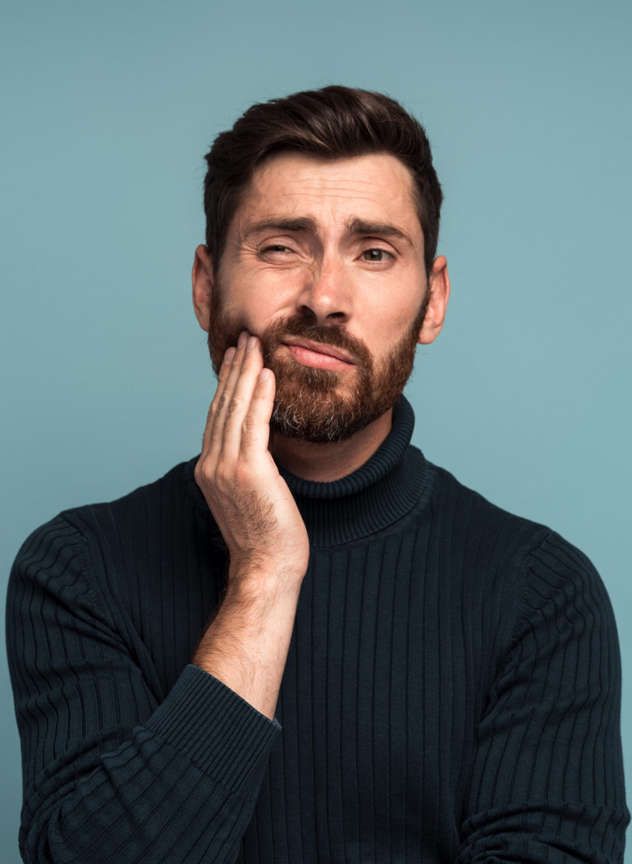Dental problems. Portrait of unhealthy man pressing sore cheek, suffering acute toothache, periodontal disease, cavities or jaw pain. Indoor studio shot isolated on blue background
