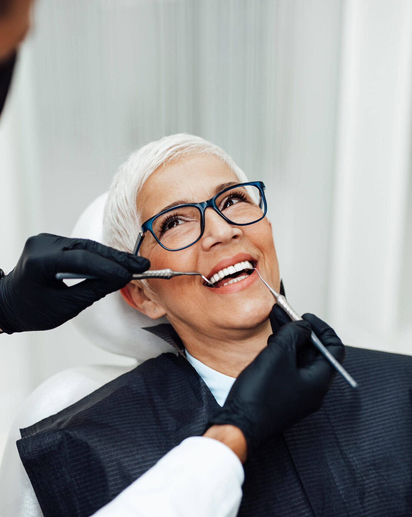 Beautiful senior woman having dental treatment at dentist's office. Dentist is wearing protective face mask due to coronavirus pandemic.