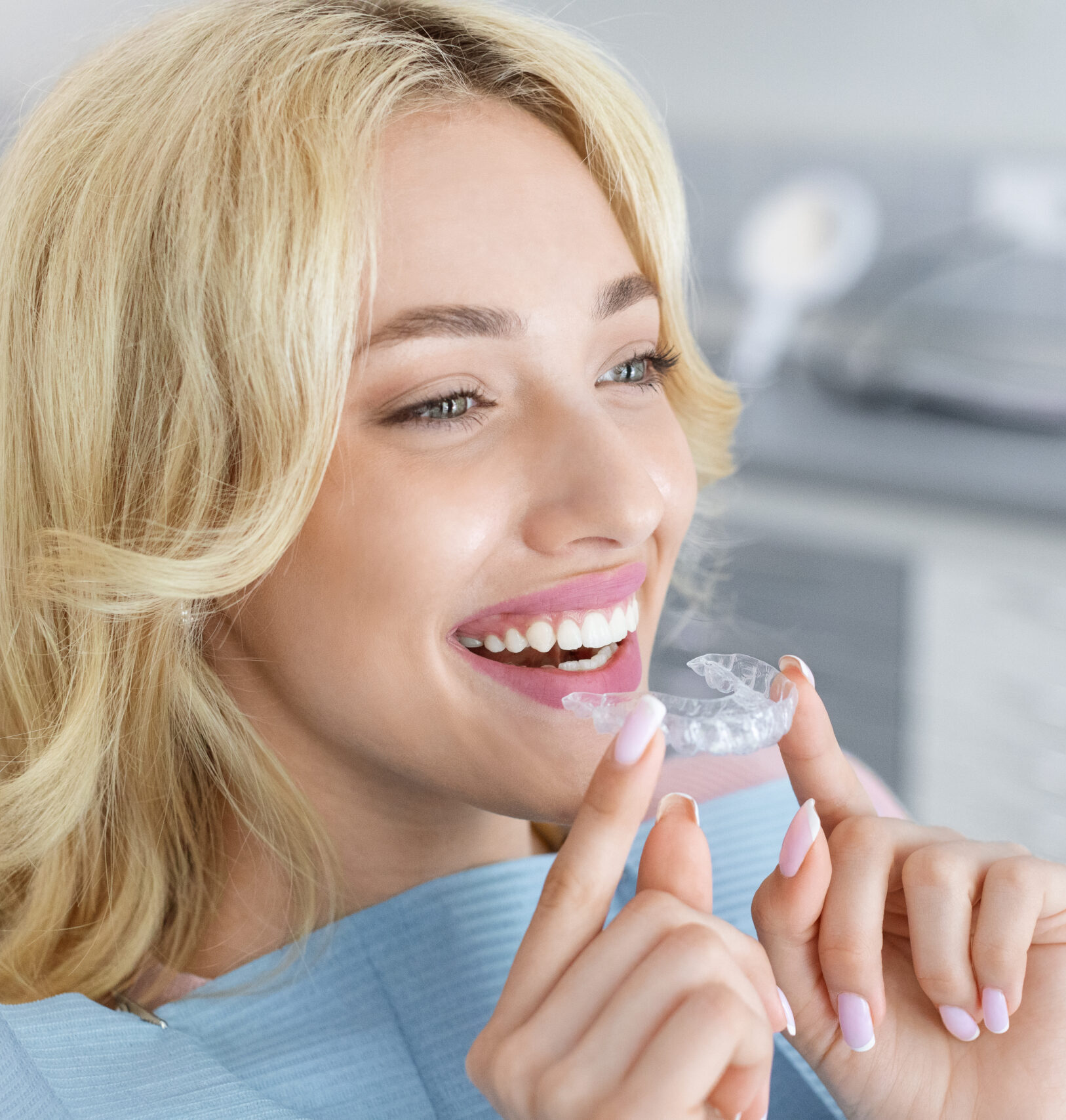 Invisalign orthodontics, modern dentistry concept. Happy young attractive blonde woman holding invisible braces or trainer while sitting at dental chair, closeup portrait, copy space