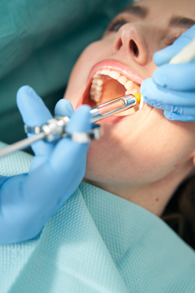 Close up of stomatologist hands in sterile gloves inserting needle into woman gum while doing local anesthesia injection before dental procedure