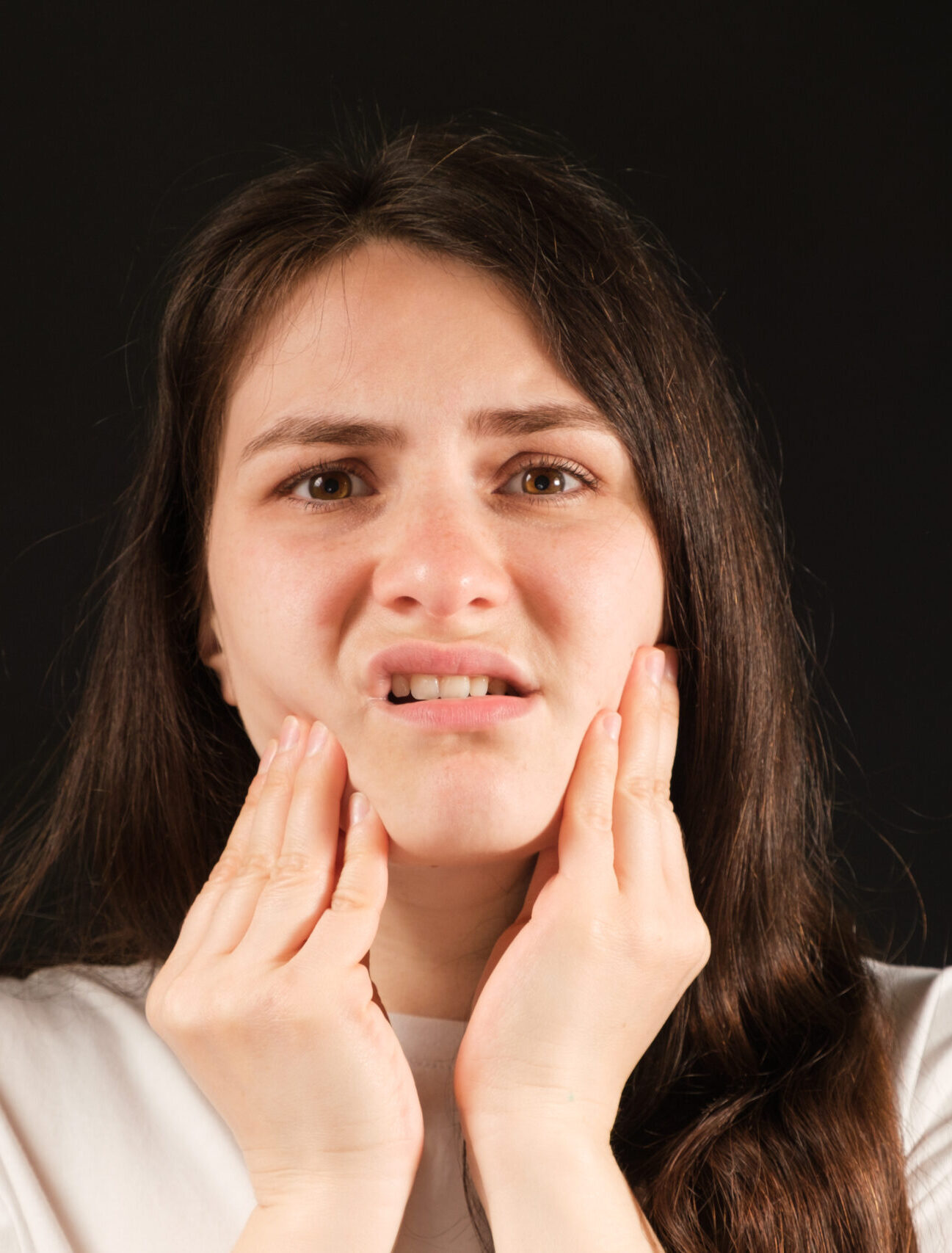 A woman holds her hands to a sore temporomandibular joint, dysfunction and pain, dislocated jaw, problems of wisdom teeth