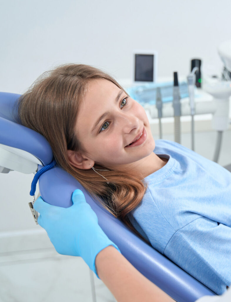 Pleased teenage patient lying in dental chair and looking at pediatric dentist
