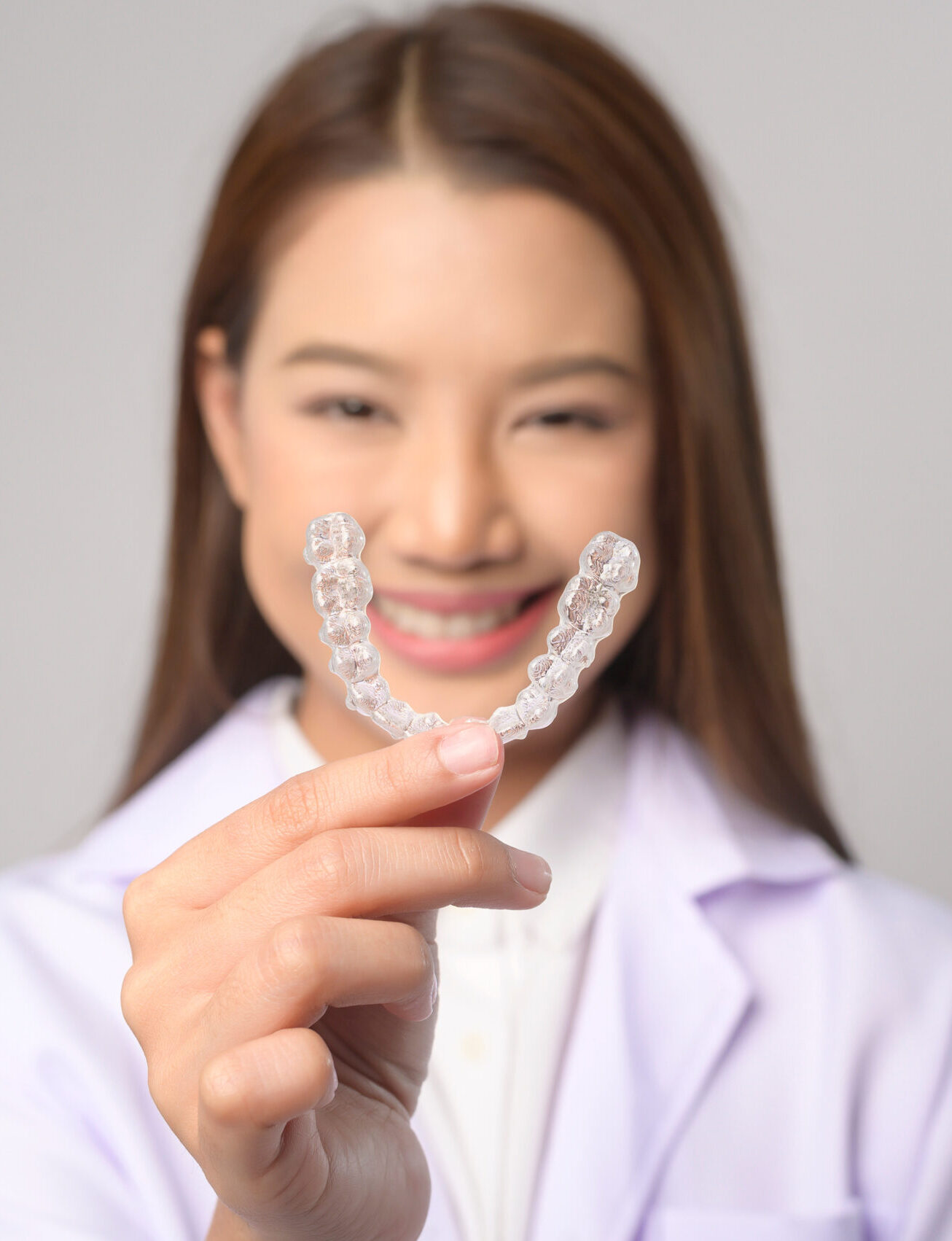 A Young female dentist holding invisalign braces over white background studio, dental healthcare and Orthodontic concept.