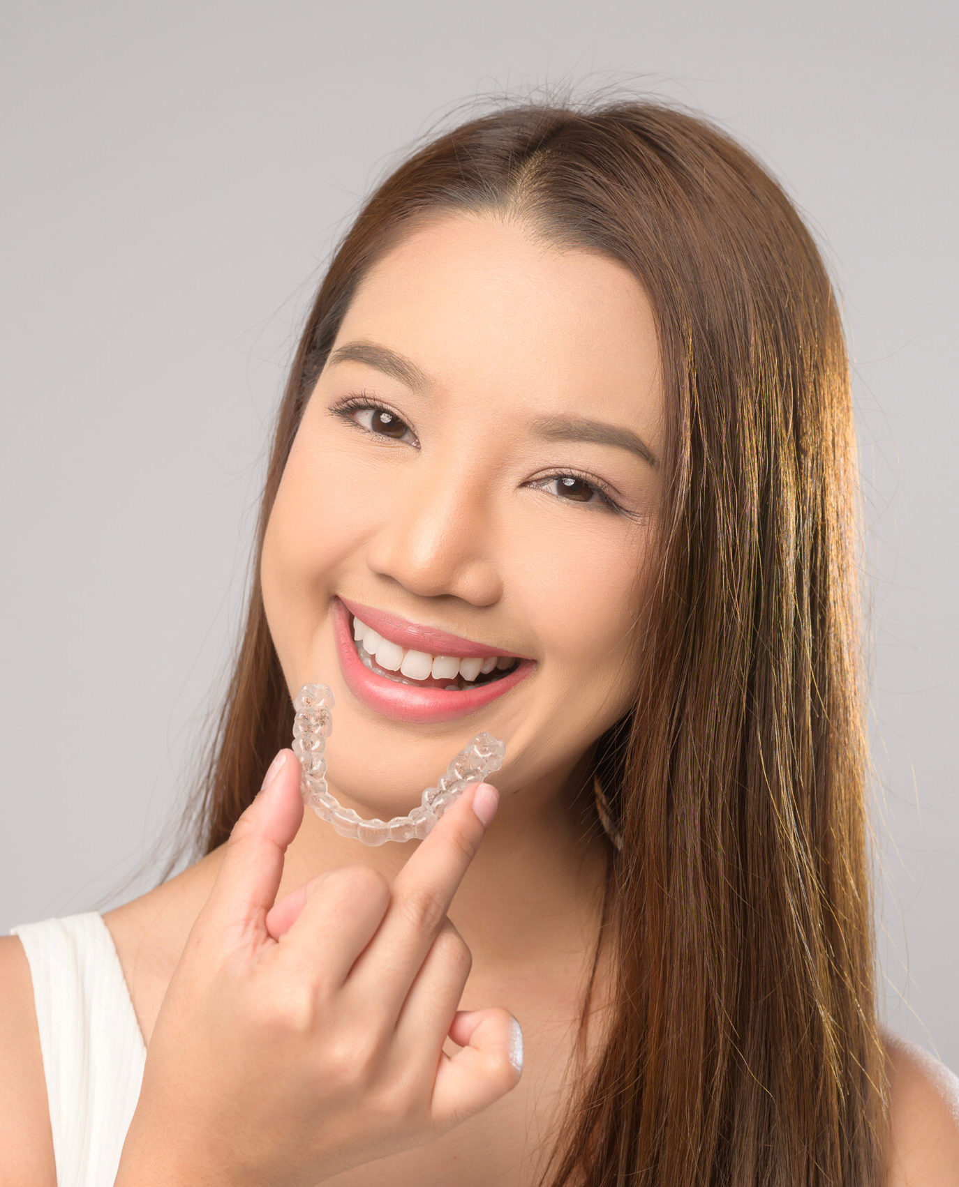 A Young smiling woman holding invisalign braces over white background studio, dental healthcare and Orthodontic concept.