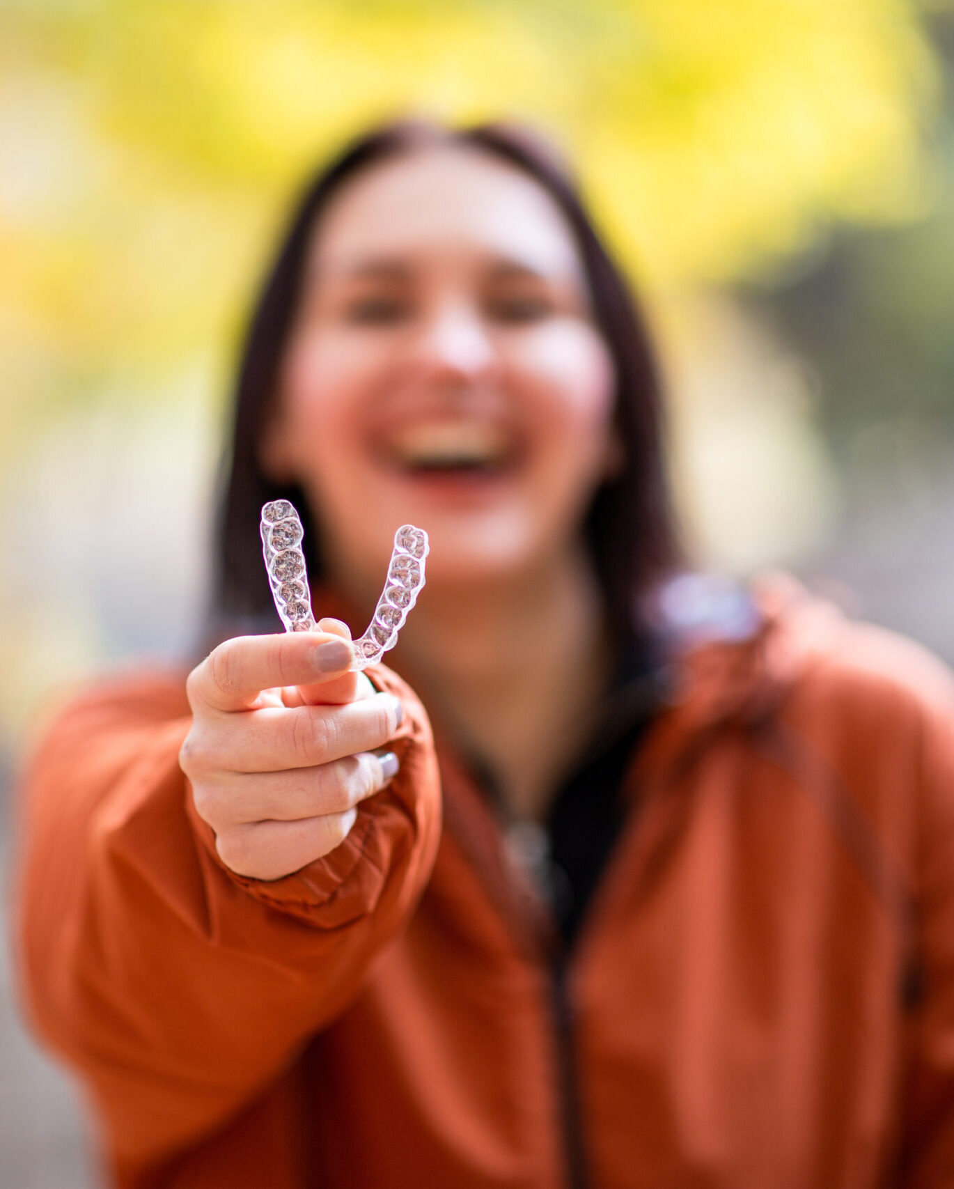 Happy young woman smiling with invisible teeth aligner during fall season at park.