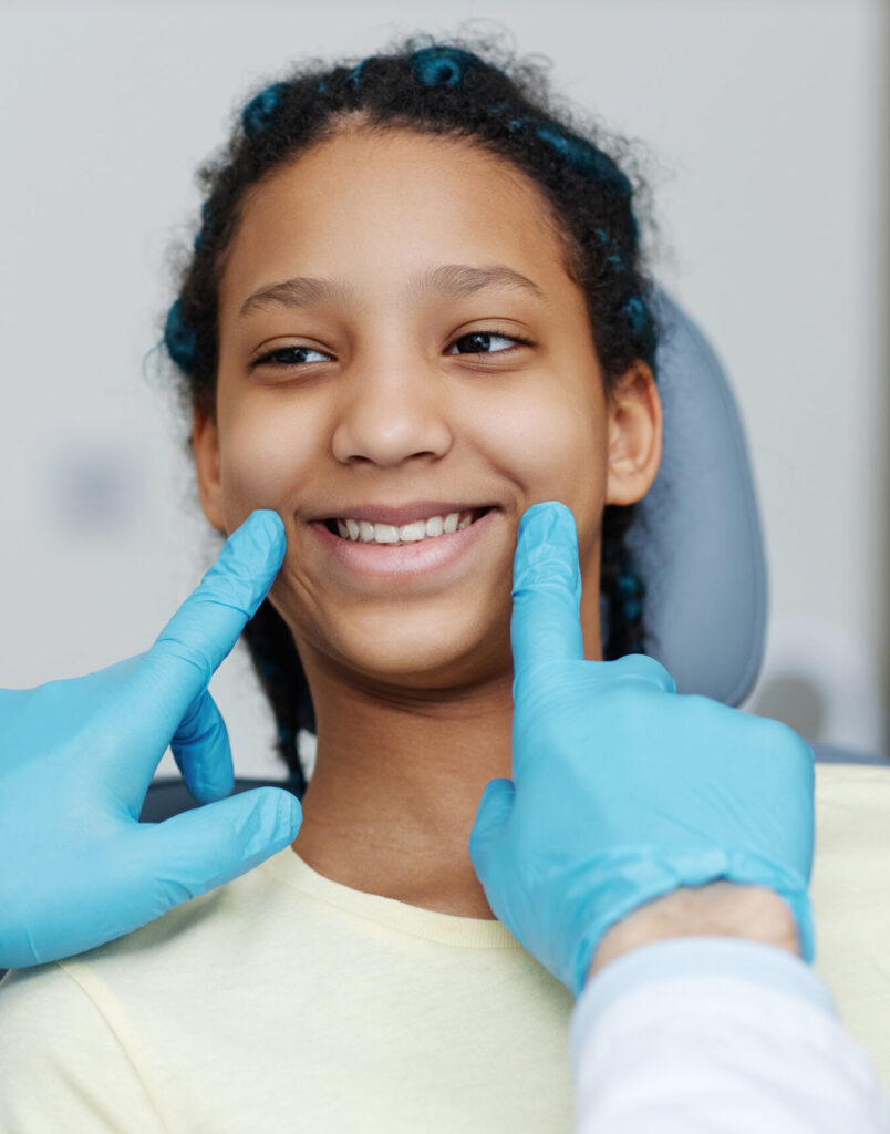 Portrait of teen black girl with toothy smile sitting in a dental chair at dentistry clinic