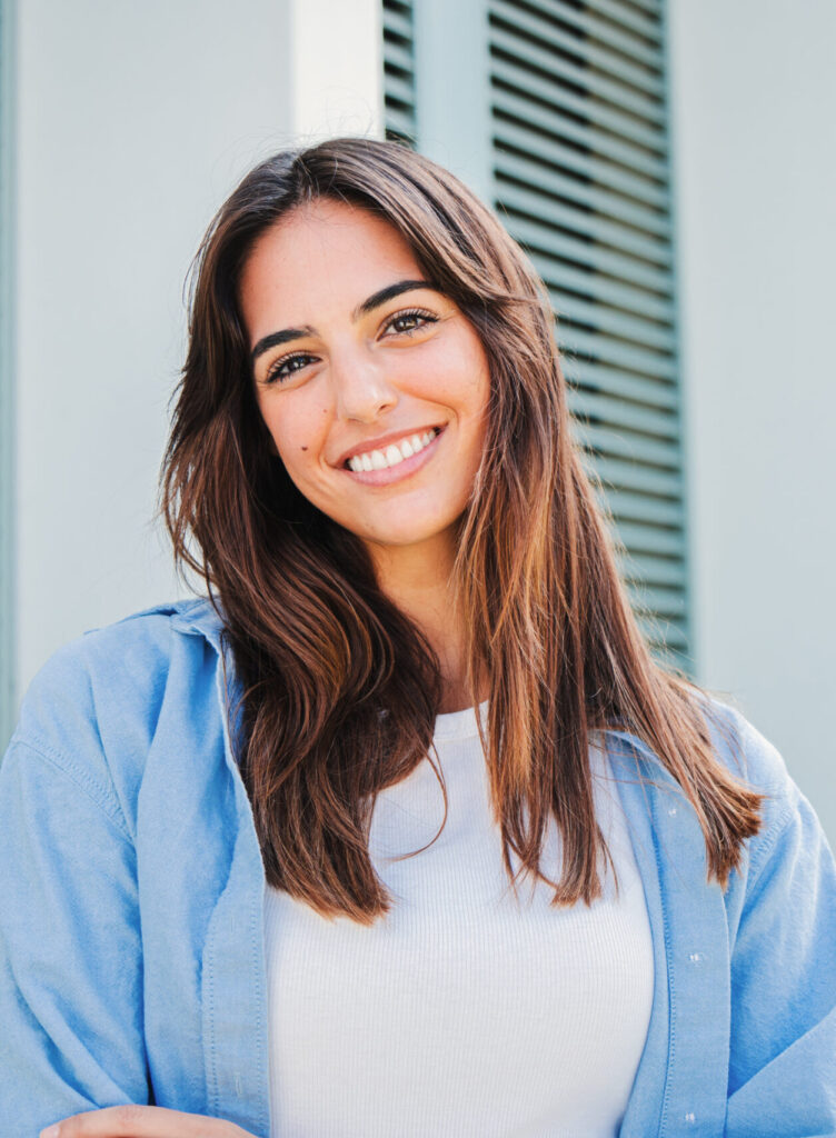 Happy caucasian young student female looking at camera enjoying with a perfect white teeth. Portrait of a joyful and adorable teenage brunette woman posing for a college promotion with crossed arms. High quality photo