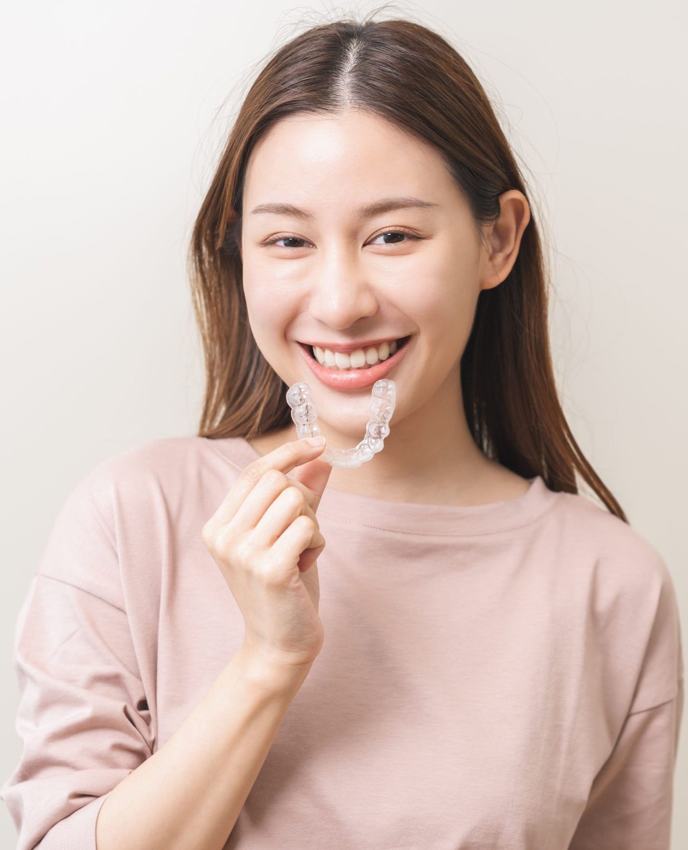 Dental invisible braces, beautiful smiling asian young woman holding invisalign braces, wearing orthodontic silicone trainer, white smile using invisible whitening tray. Stomatology, dental healthcare
