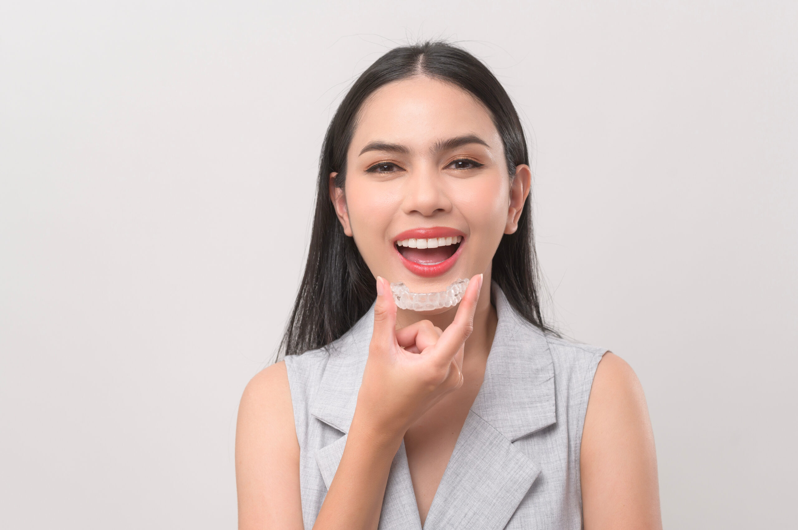 Young smiling woman holding invisalign braces in studio, dental healthcare and Orthodontic concept