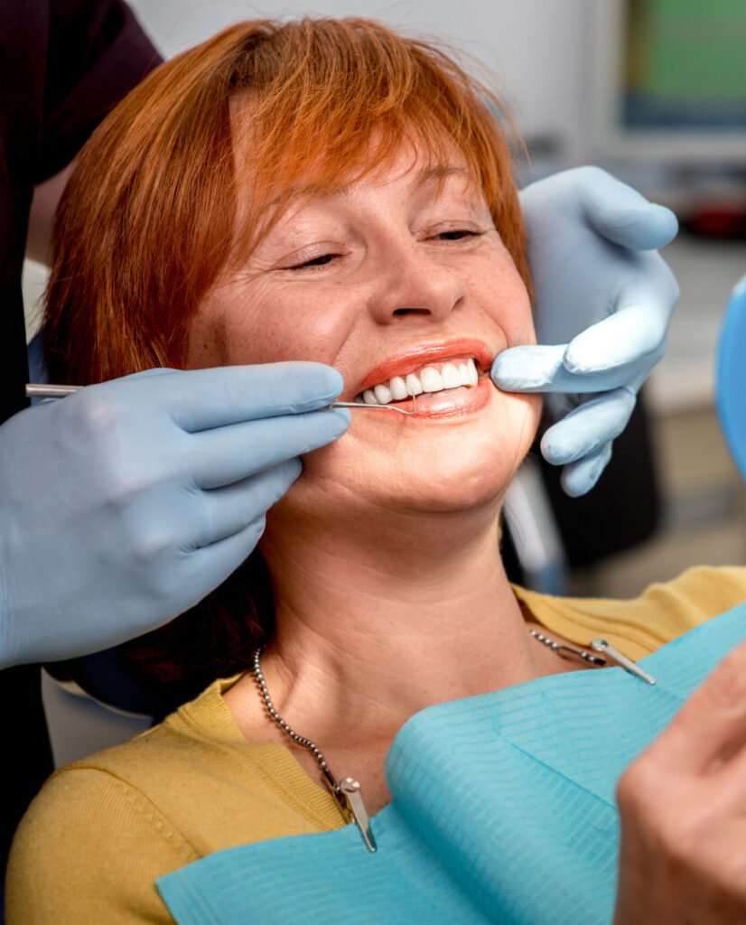 Smiling senior woman with new dental implants sitting in the dental office and looking at the mirror