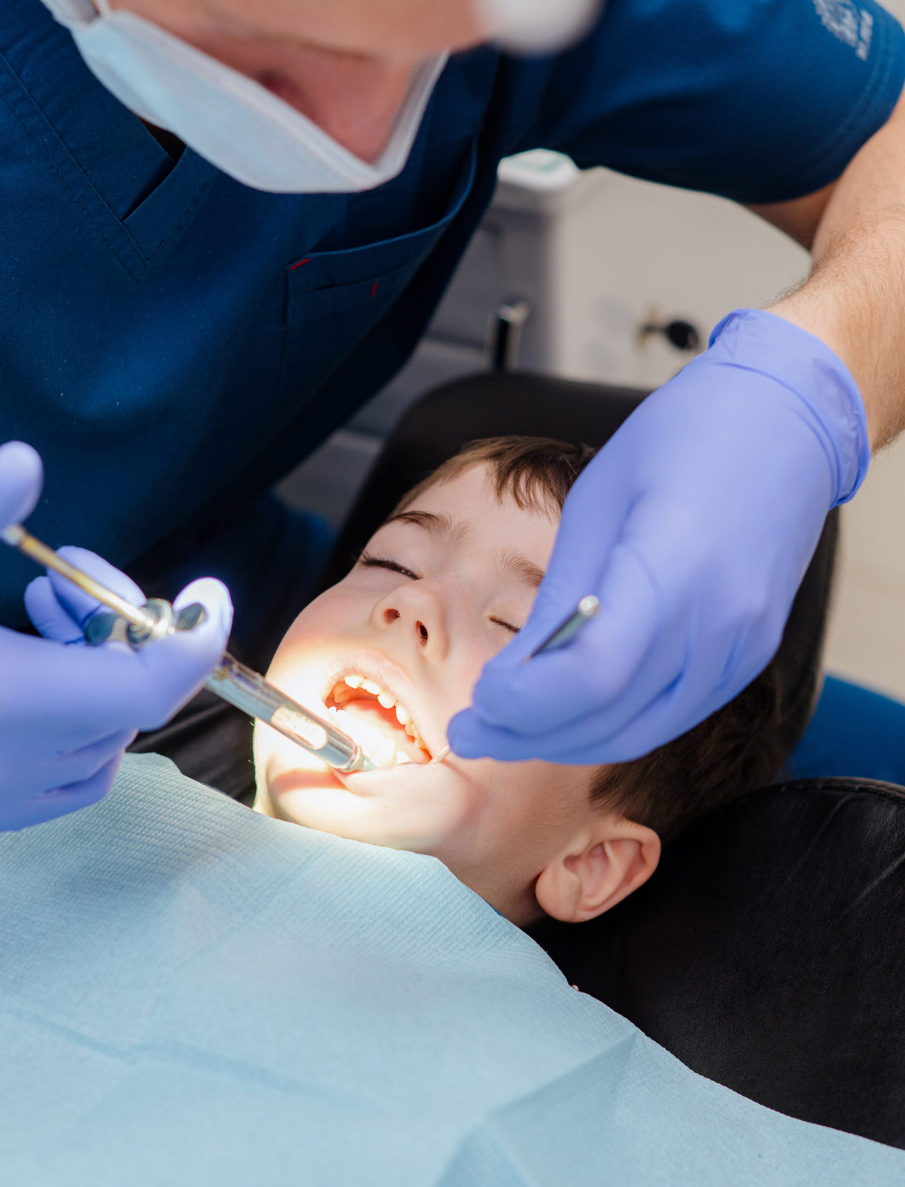The dentist checks teeth of boy who is sitting in a dental chair. Dental treatment.