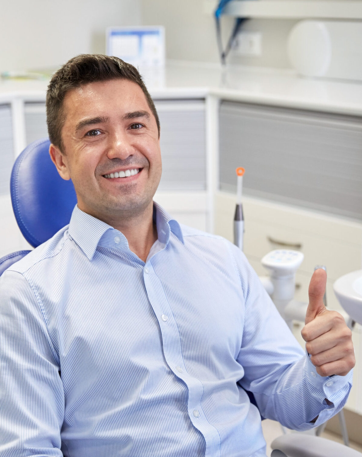 people, medicine, stomatology and health care concept - happy male patient sitting on dental chair and showing thumbs up at clinic office